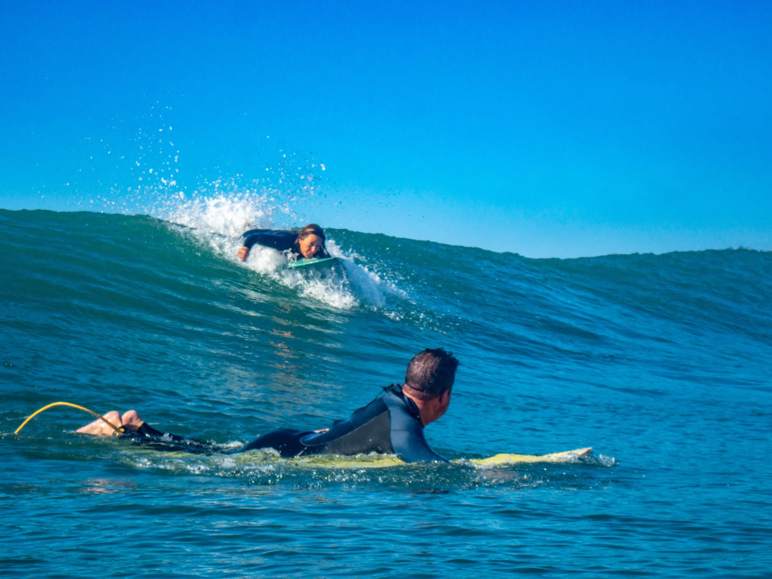 A person surfing on a wave while another person is paddling on a surfboard in the water.