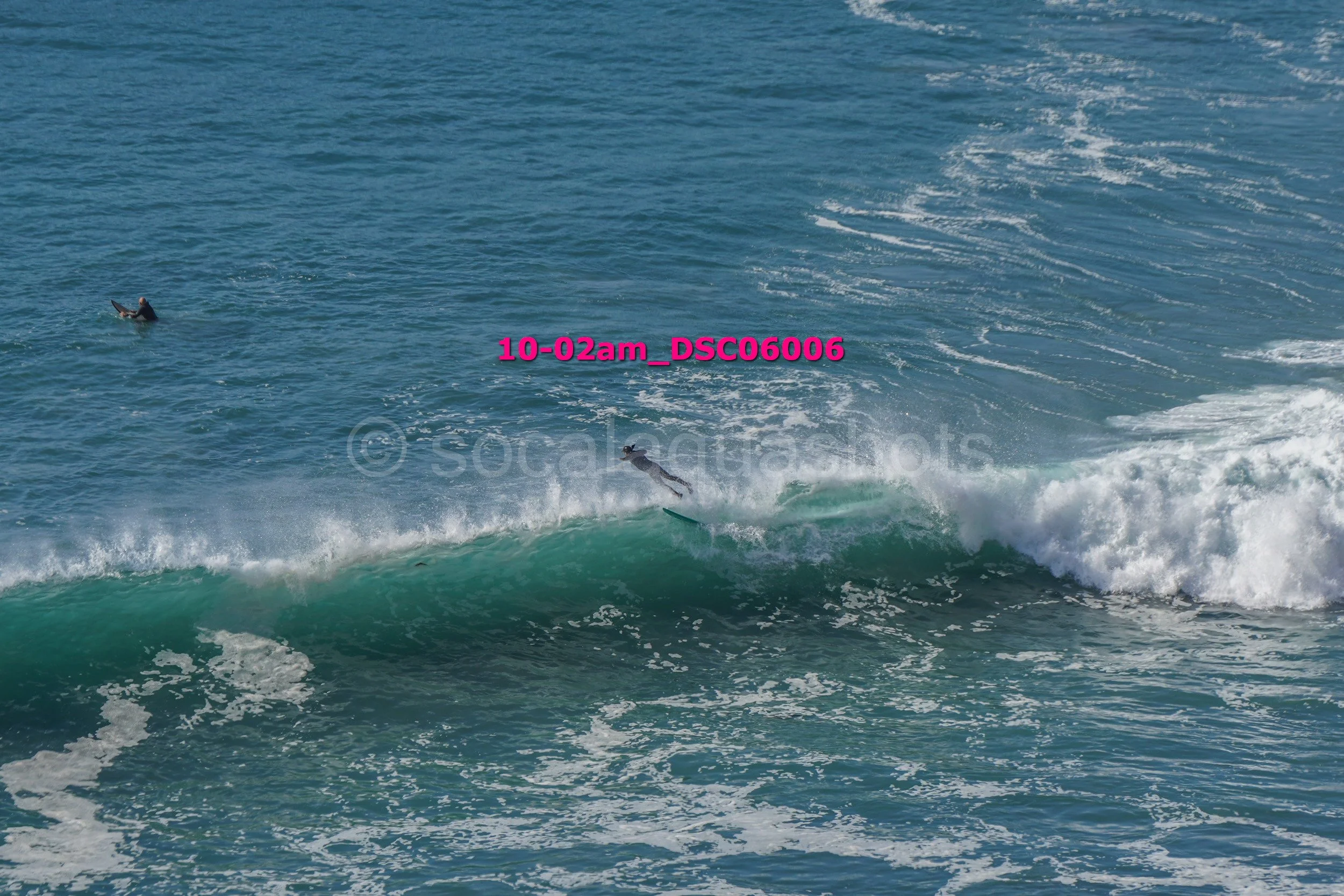 A person surfing on a wave in the ocean with another person in the water nearby.
