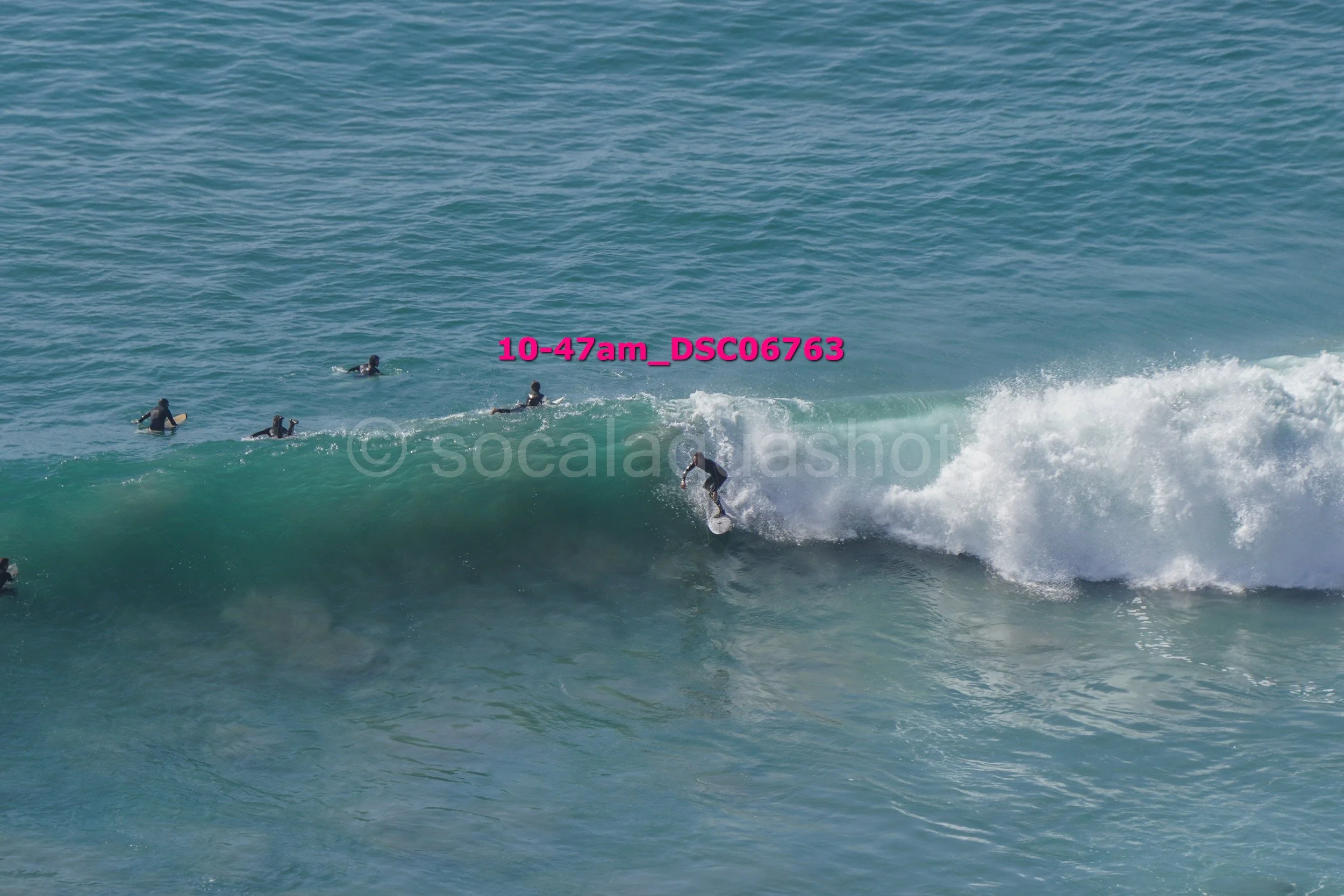 A surfer riding a wave with several other surfers waiting in the water behind.