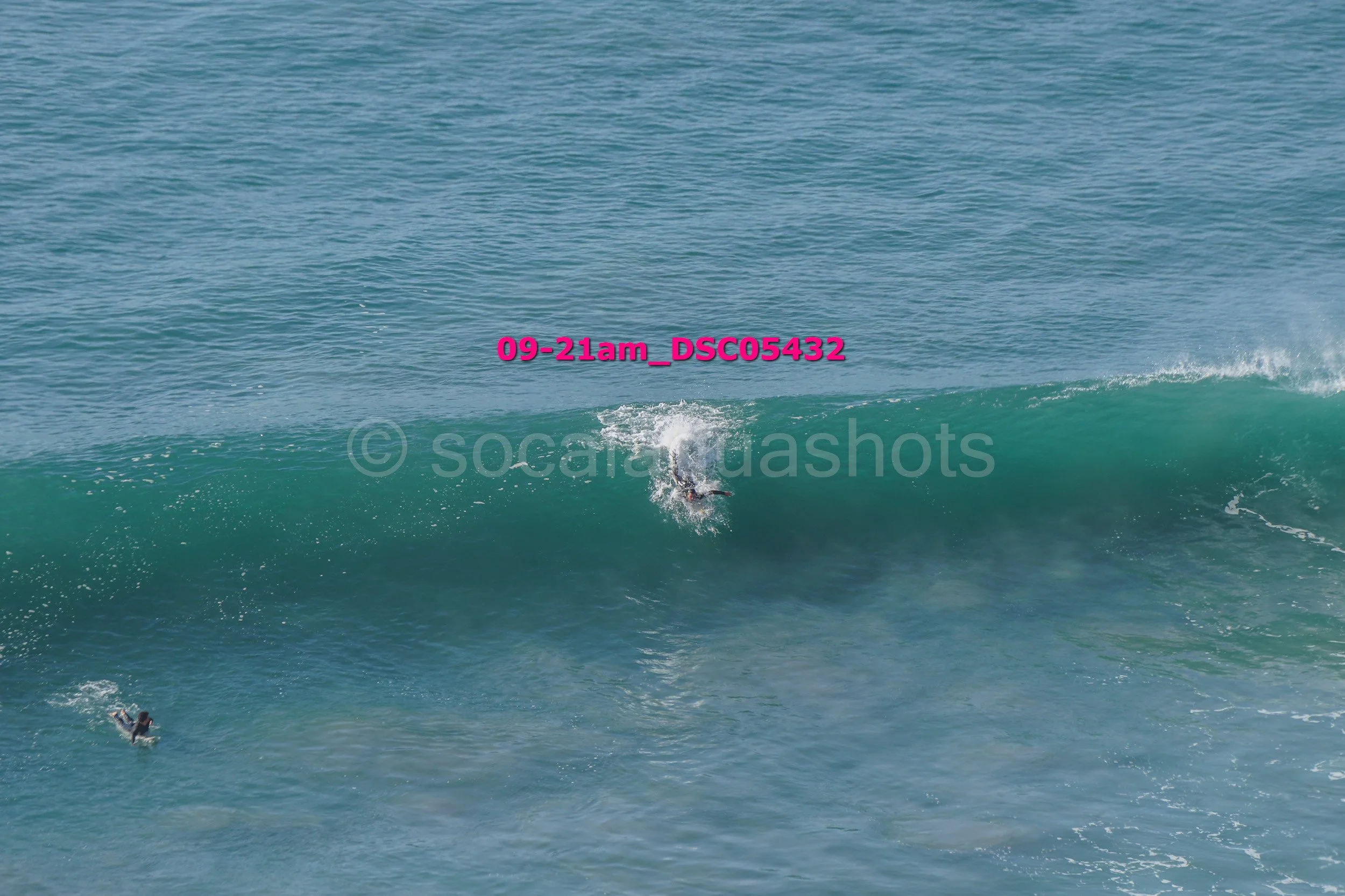 A surfer riding a large wave in the ocean, with two other surfers in the water nearby.