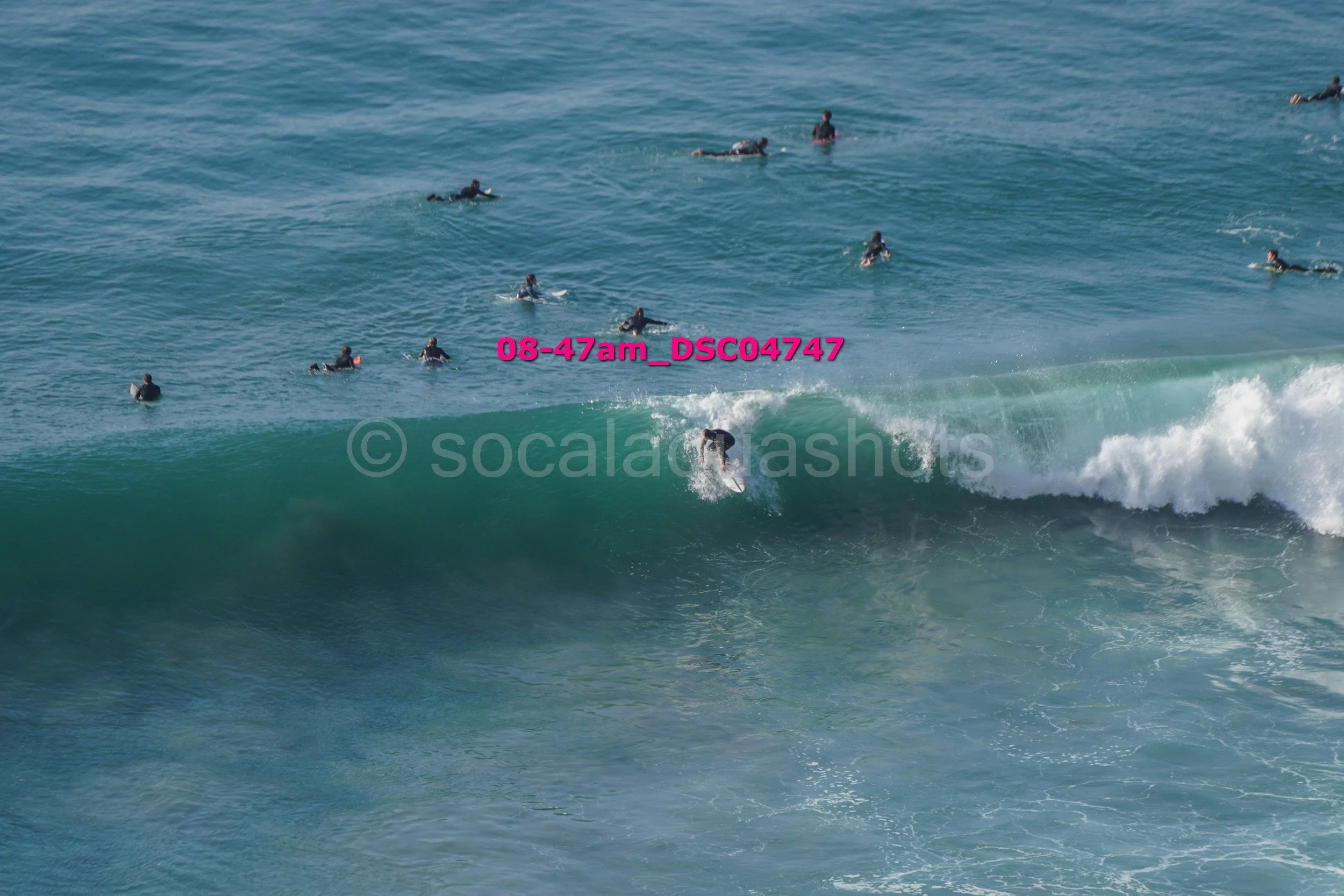 A person surfing on a wave with multiple people swimming and surfing in the background in the ocean.