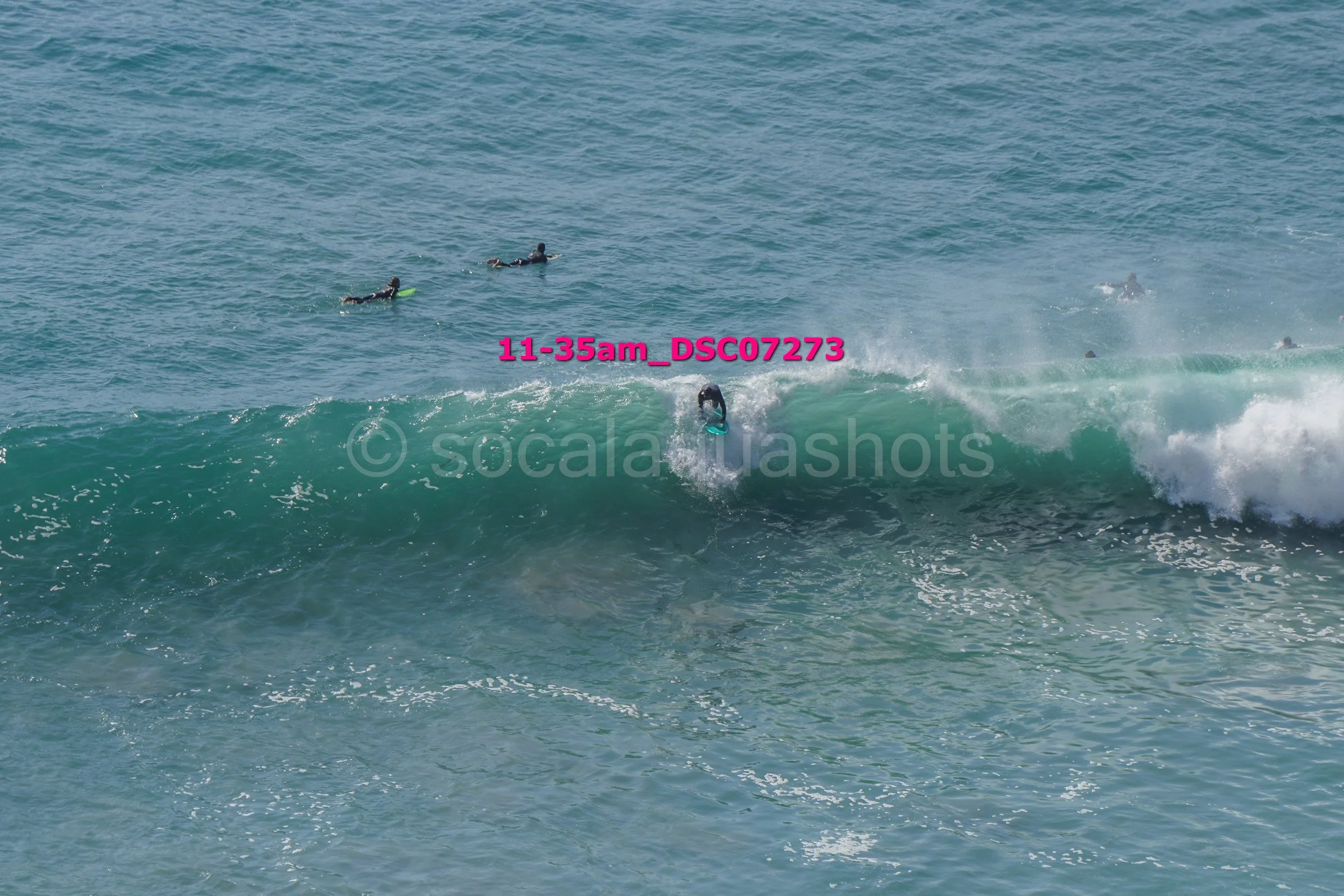 Surfer riding a wave with several people in the water in the background.