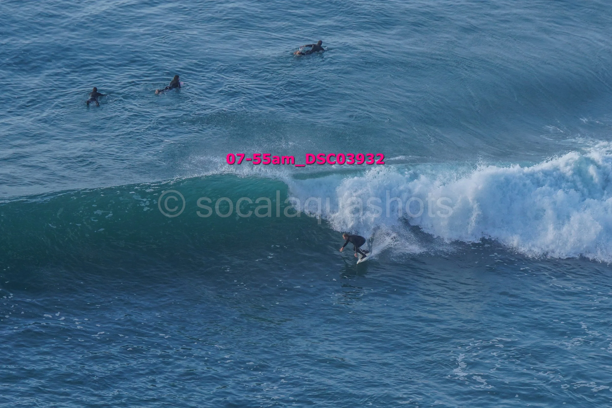 A person surfing on a wave while four others are swimming in the water nearby.