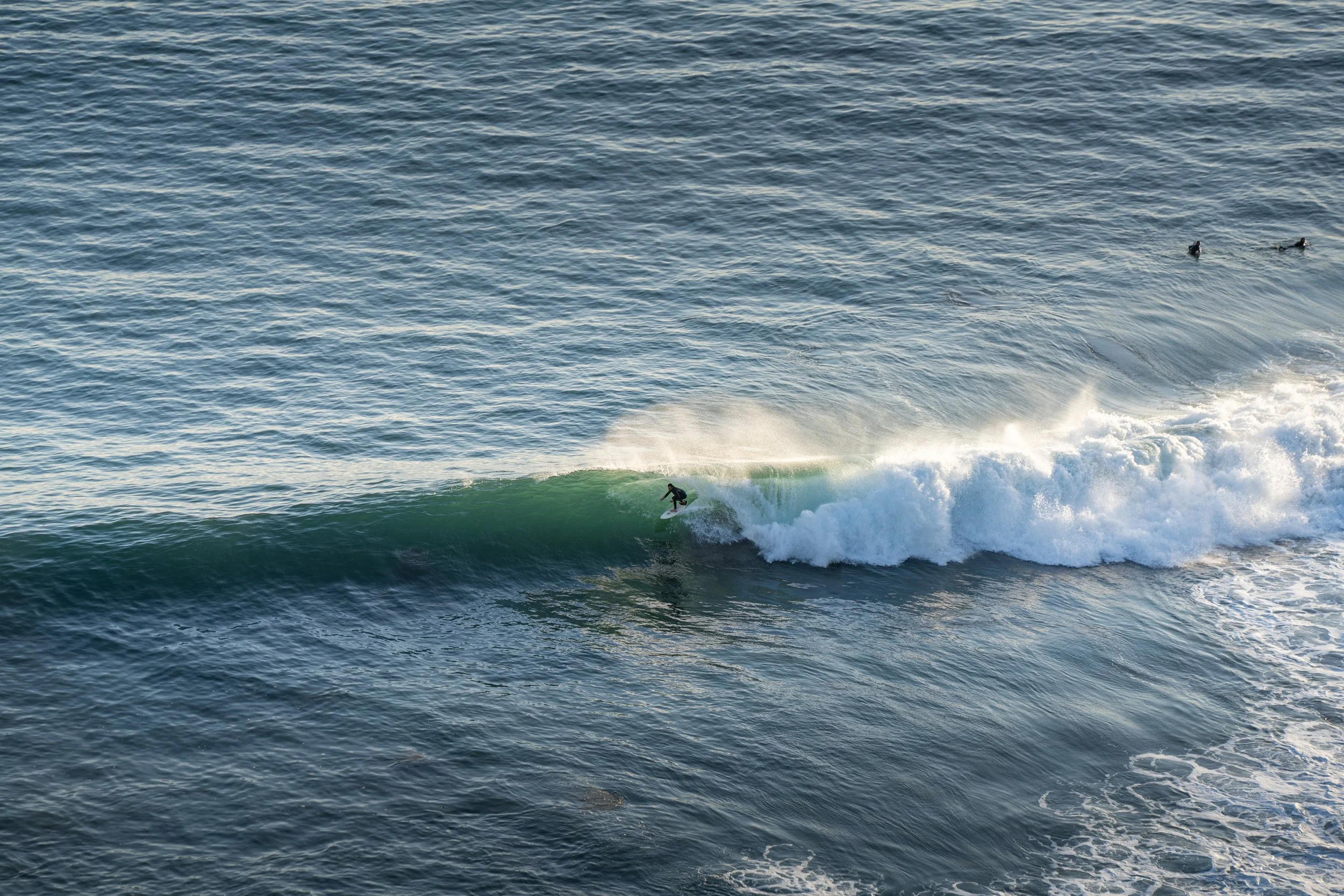A person surfing on a wave in the ocean with a few other surfers visible in the distance.