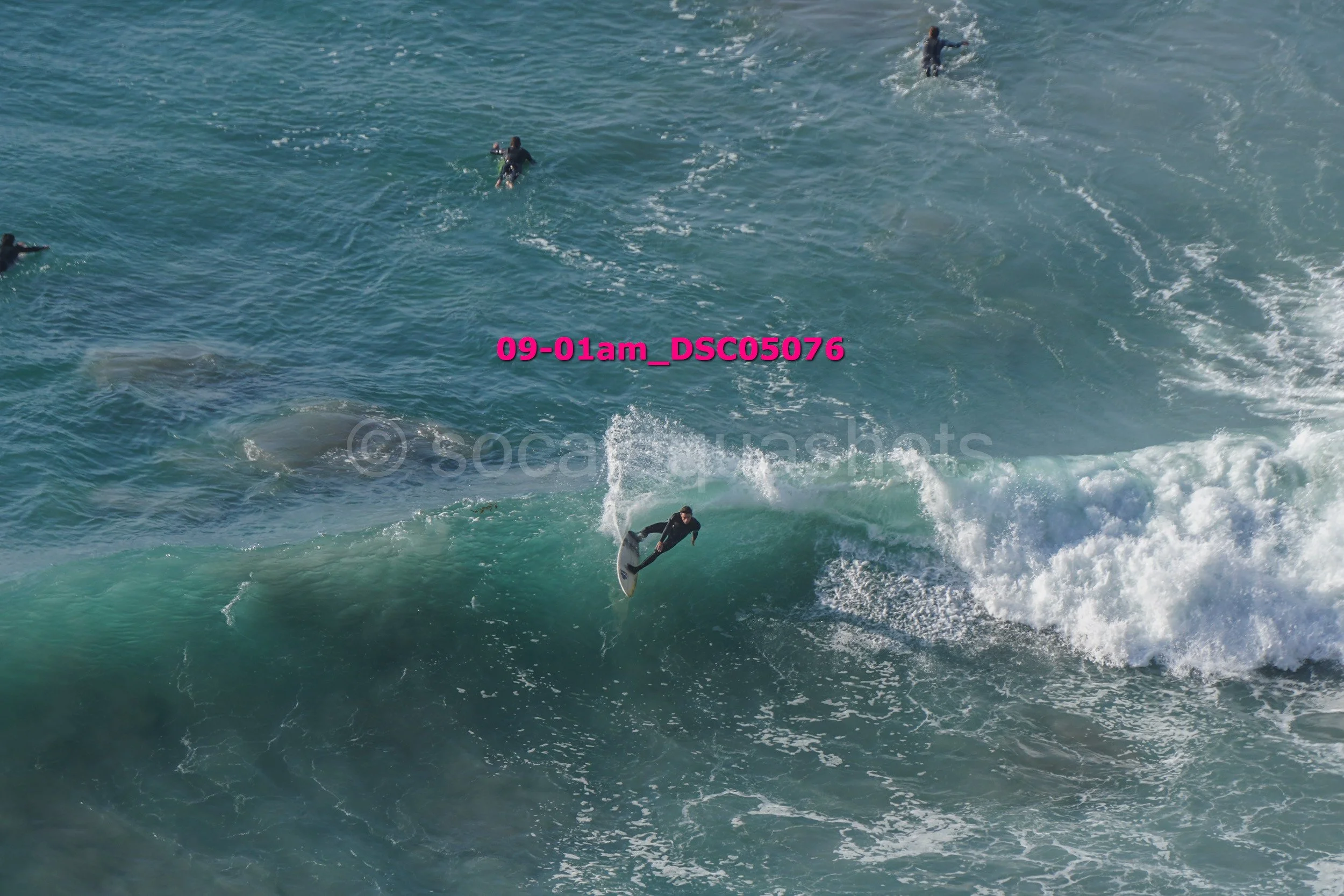 Surfer riding a wave with other surfers in the water and the ocean.