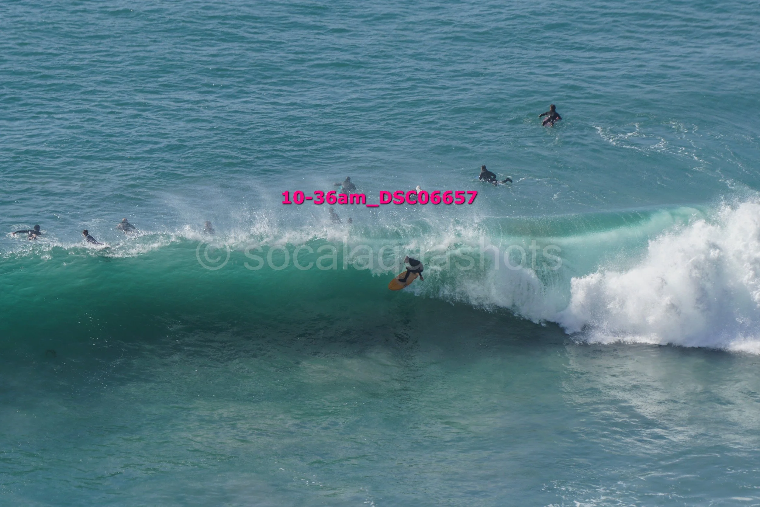 Surfer riding a wave at the beach with other surfers in the background.