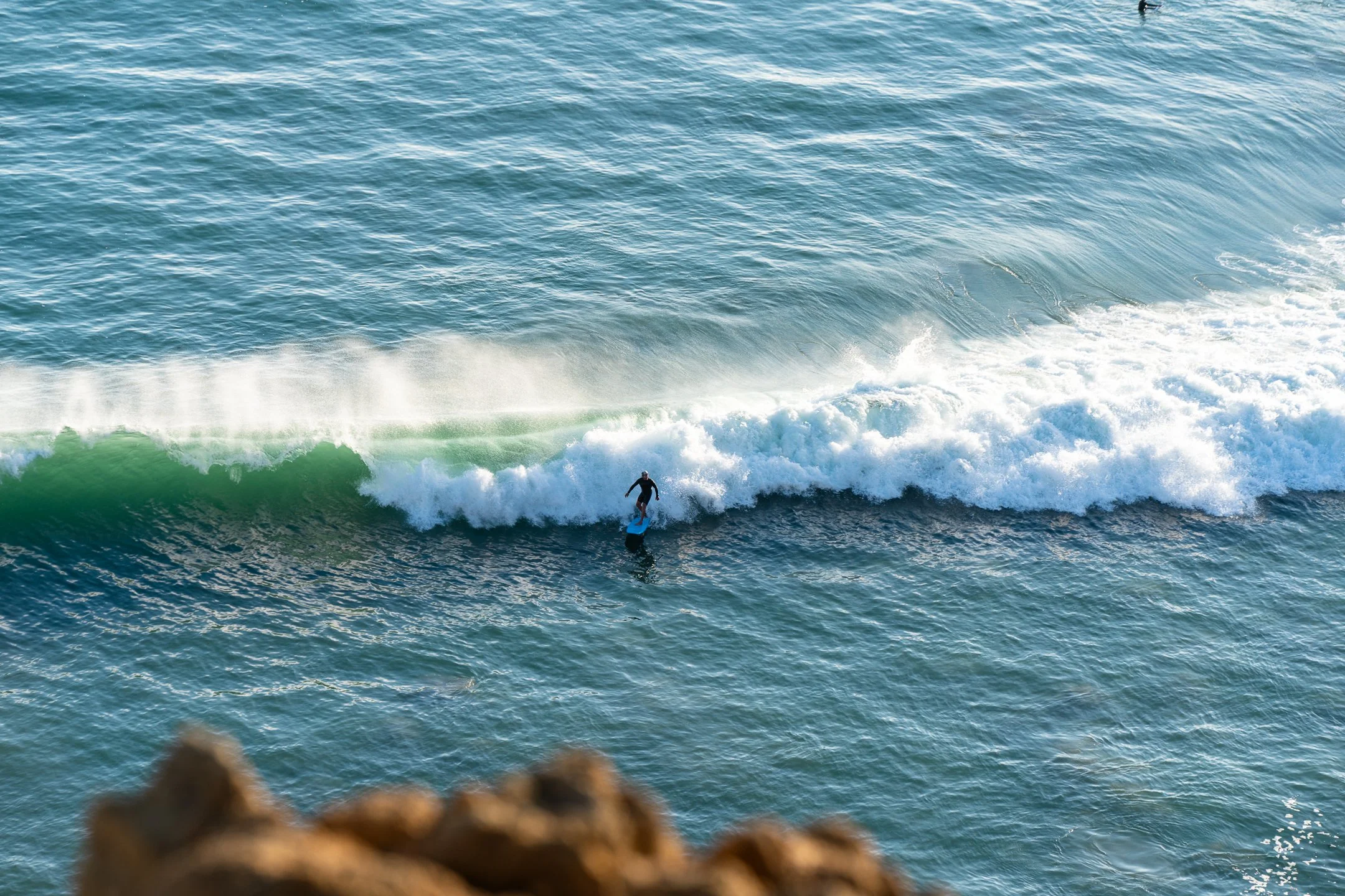 A person surfing on a wave in the ocean with another person in the water nearby, seen from a high angle.