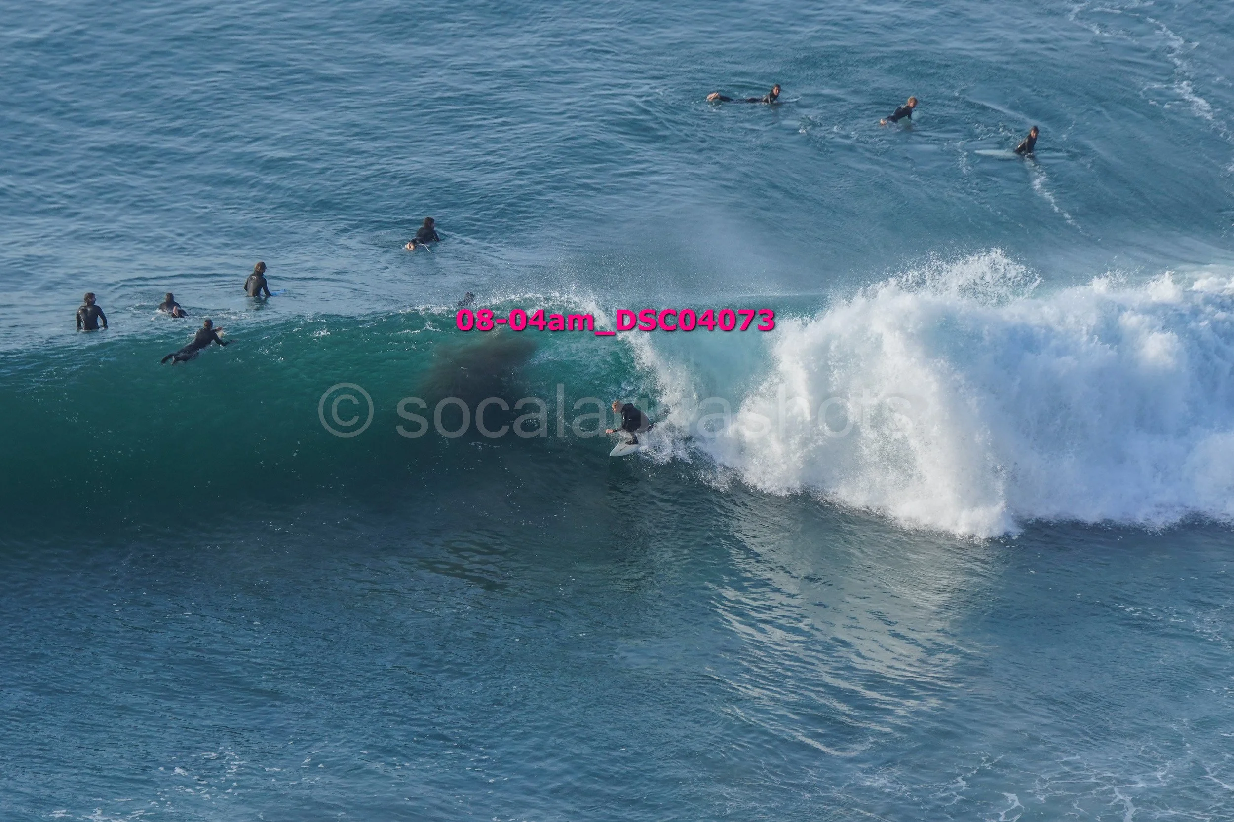 A group of people in the ocean, some swimming and one person surfing a large wave.