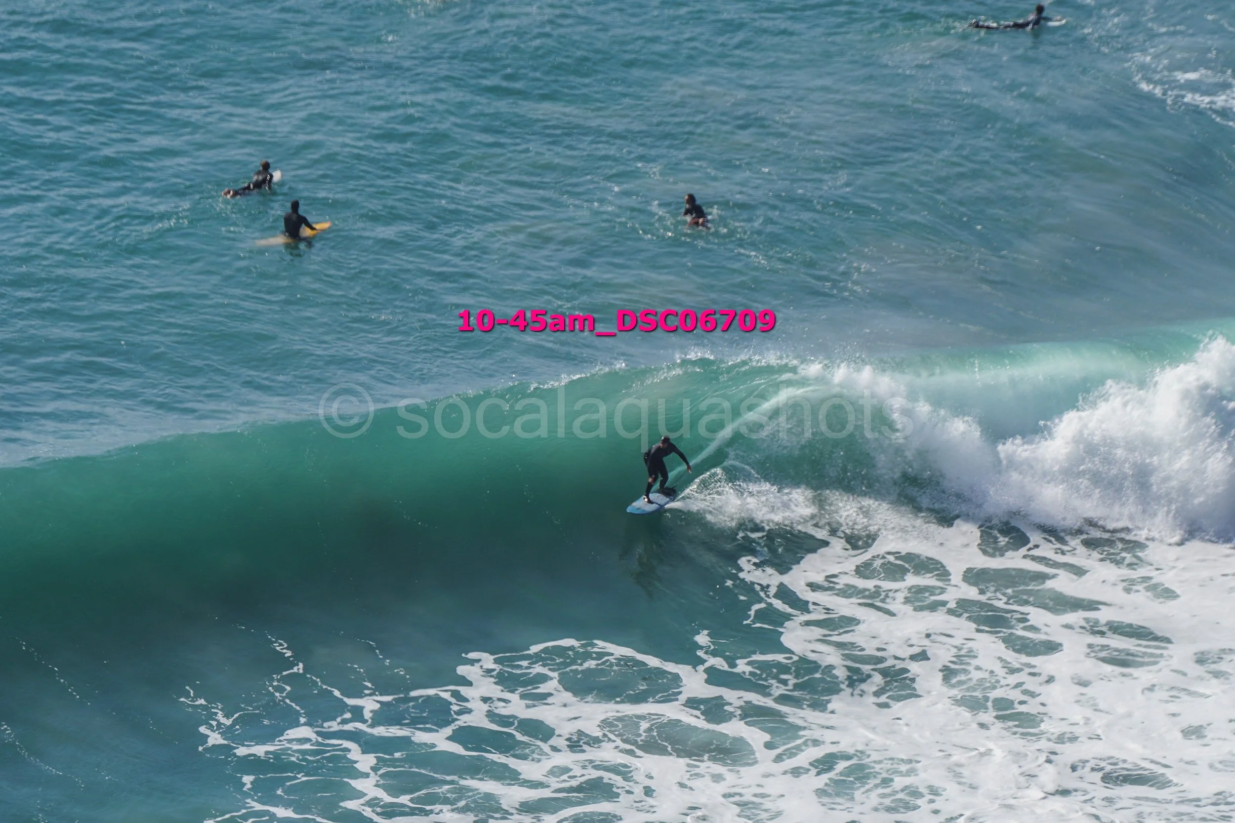 A person surfing on a wave with four other surfers in the water nearby.