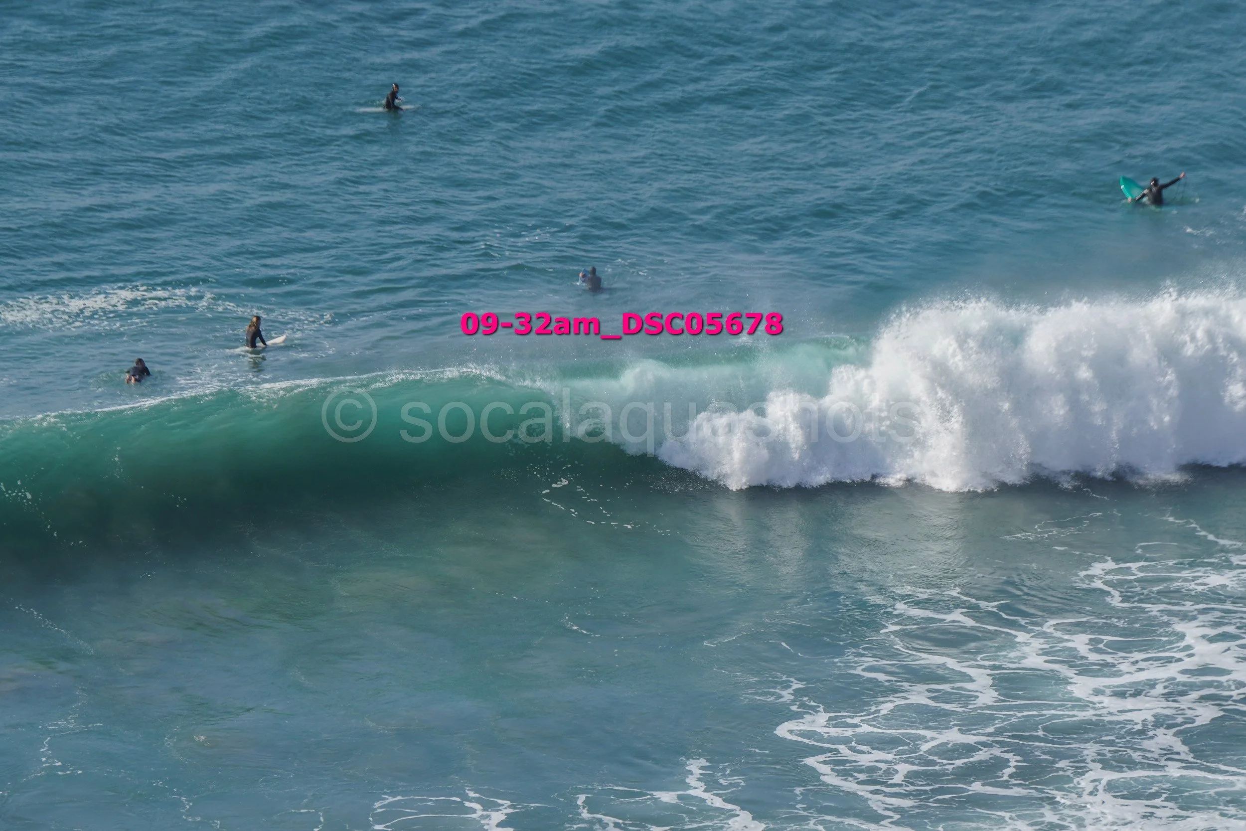 Several surfers in wetsuits riding and waiting for waves in the ocean.