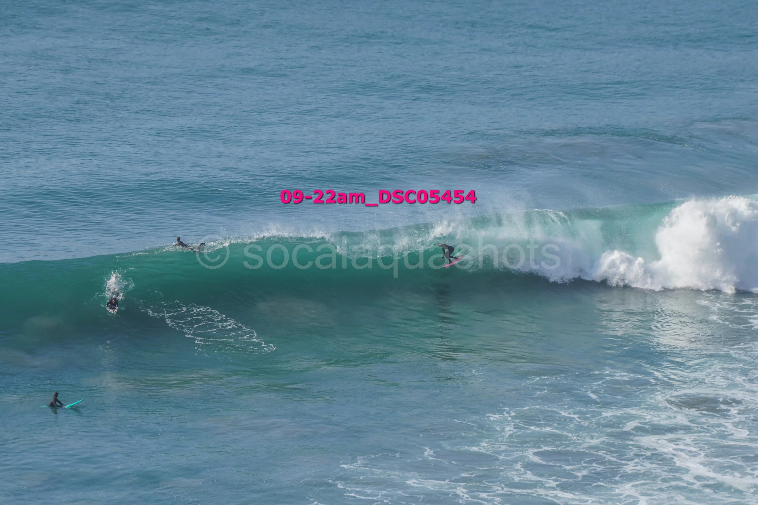 Multiple surfers riding a large ocean wave with one surfer paddling nearby, with the scene labeled '09-22am_DSC05454'
