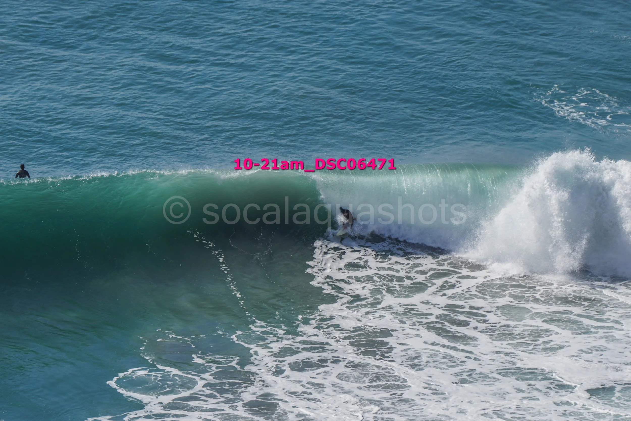 A person surfing on a large wave in the ocean with another person swimming in the background