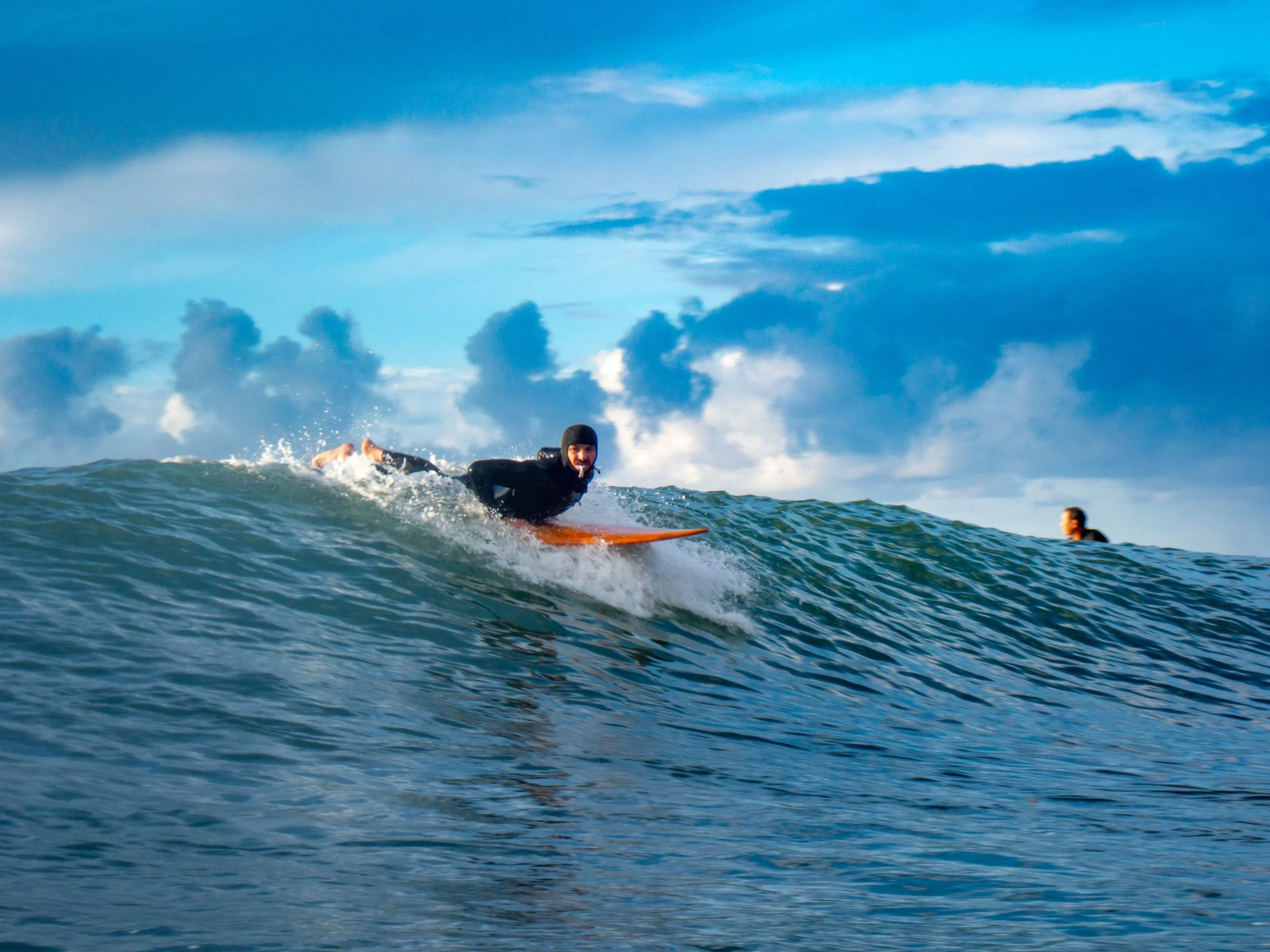 A person surfing on a wave in the ocean with a partly cloudy sky in the background.