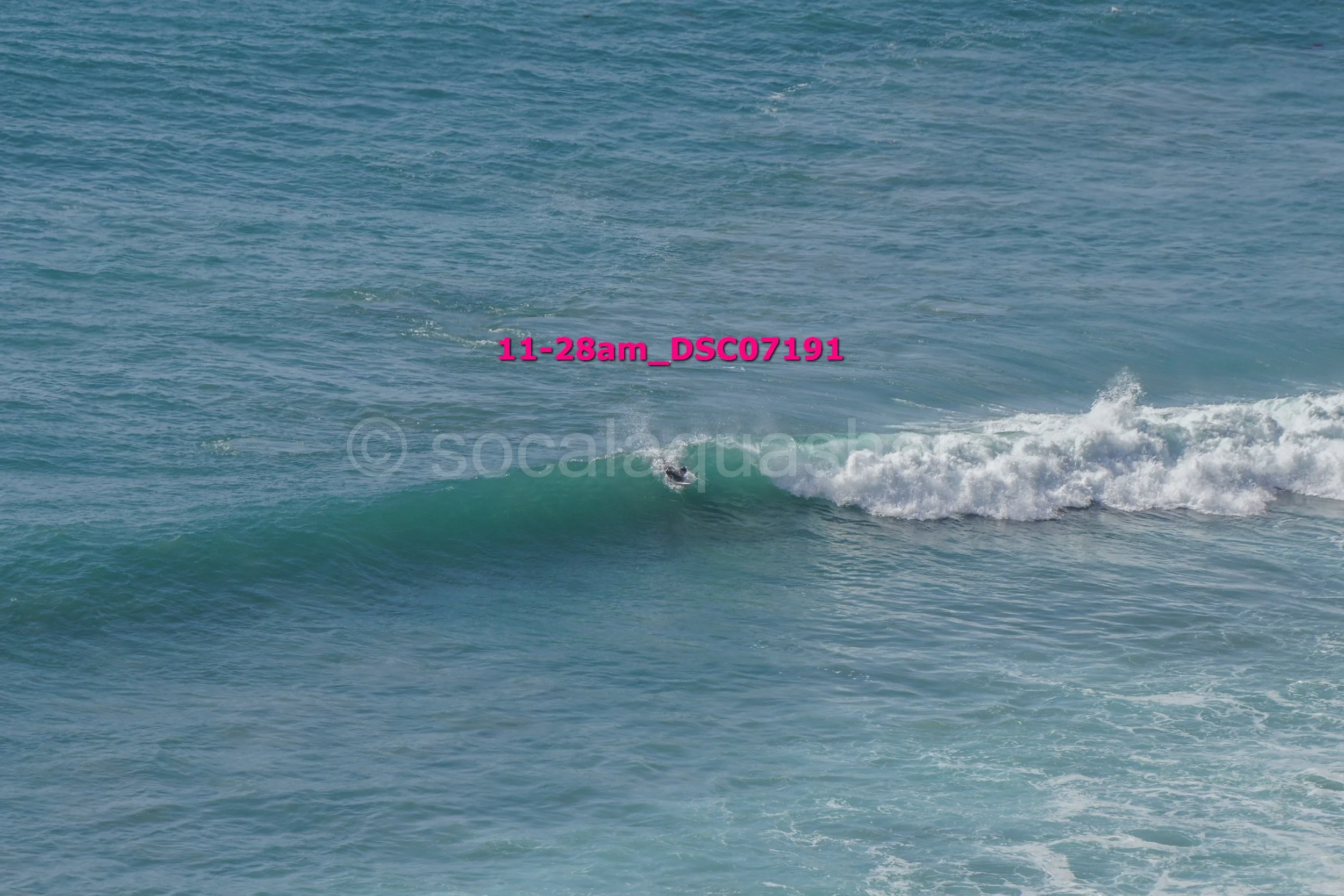 A person surfing on a small wave in the ocean with a clear blue sky.