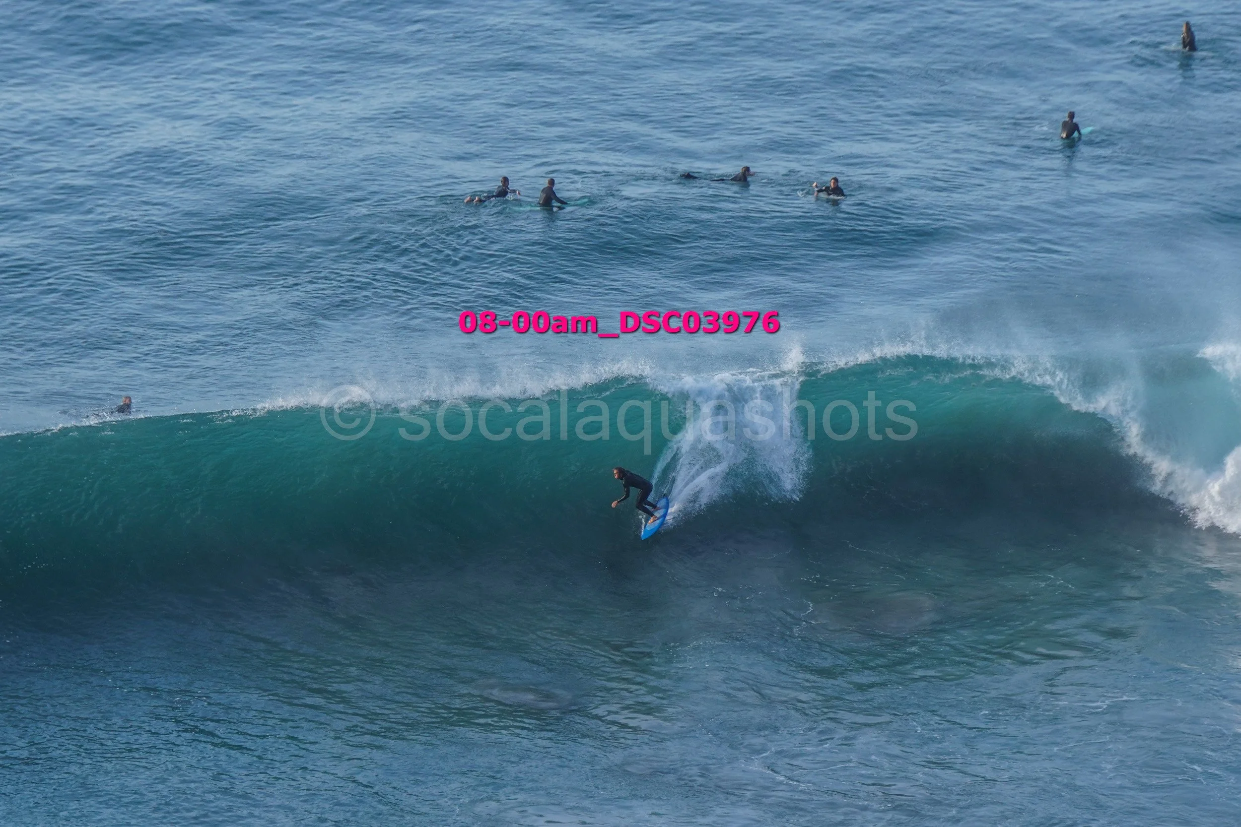A person surfing a large wave with several surfers in the water in the background.