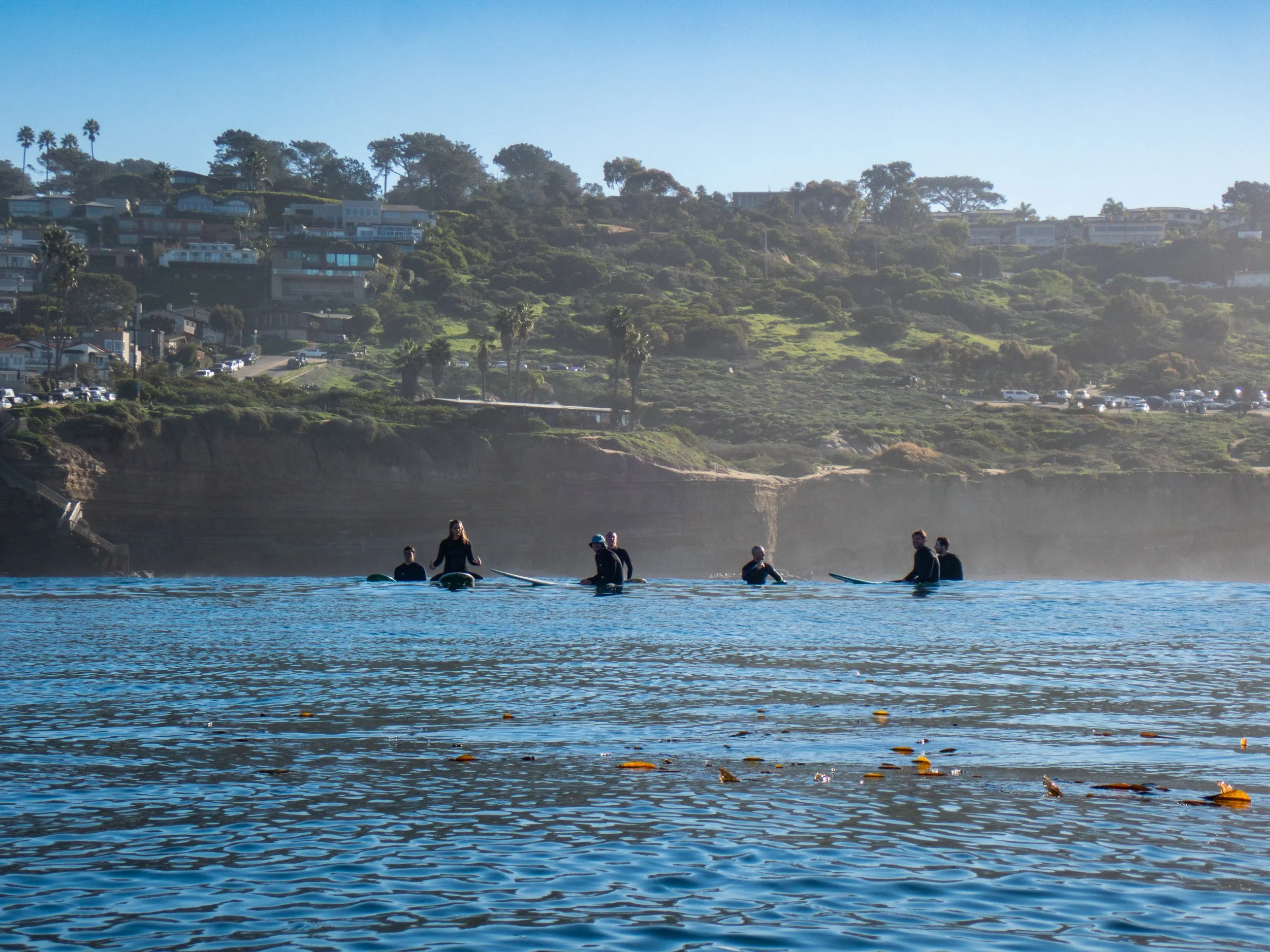 Group of five people paddleboarding on the water with a cityscape and hillside in the background.