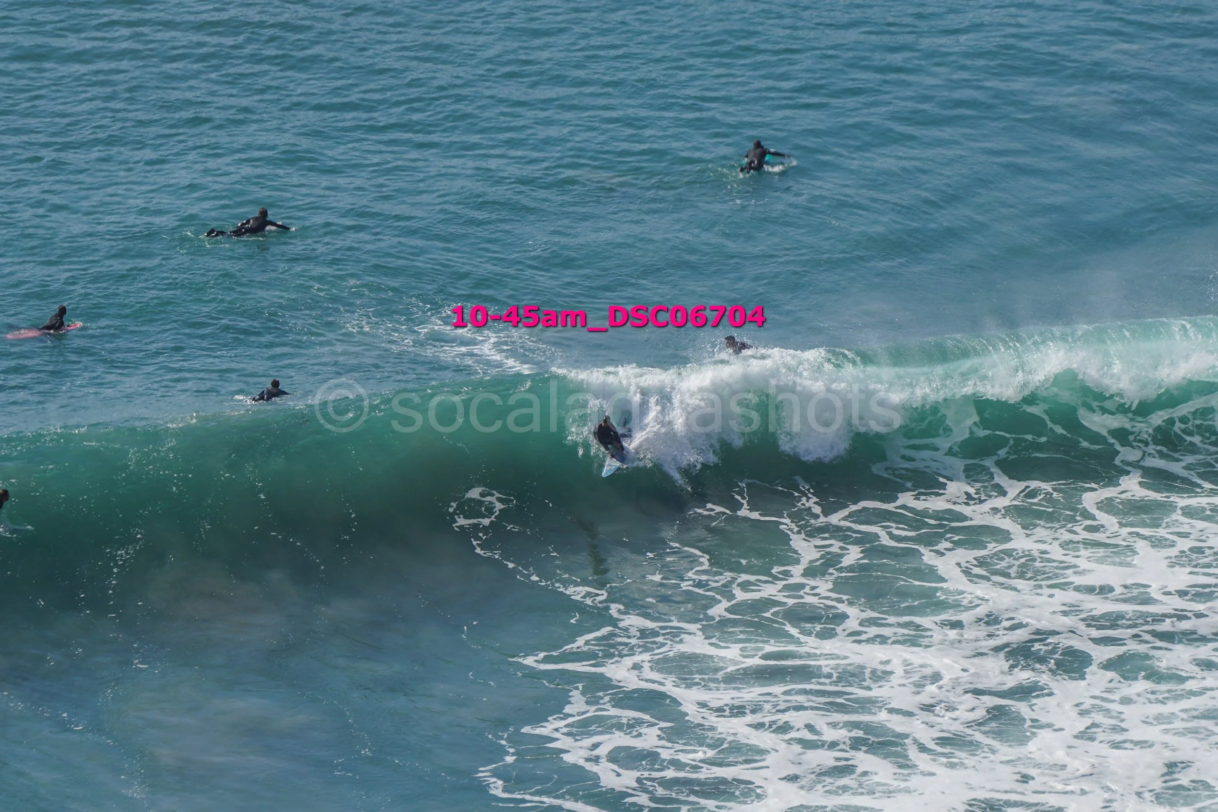 Surfer riding a wave with several people swimming in the ocean nearby.