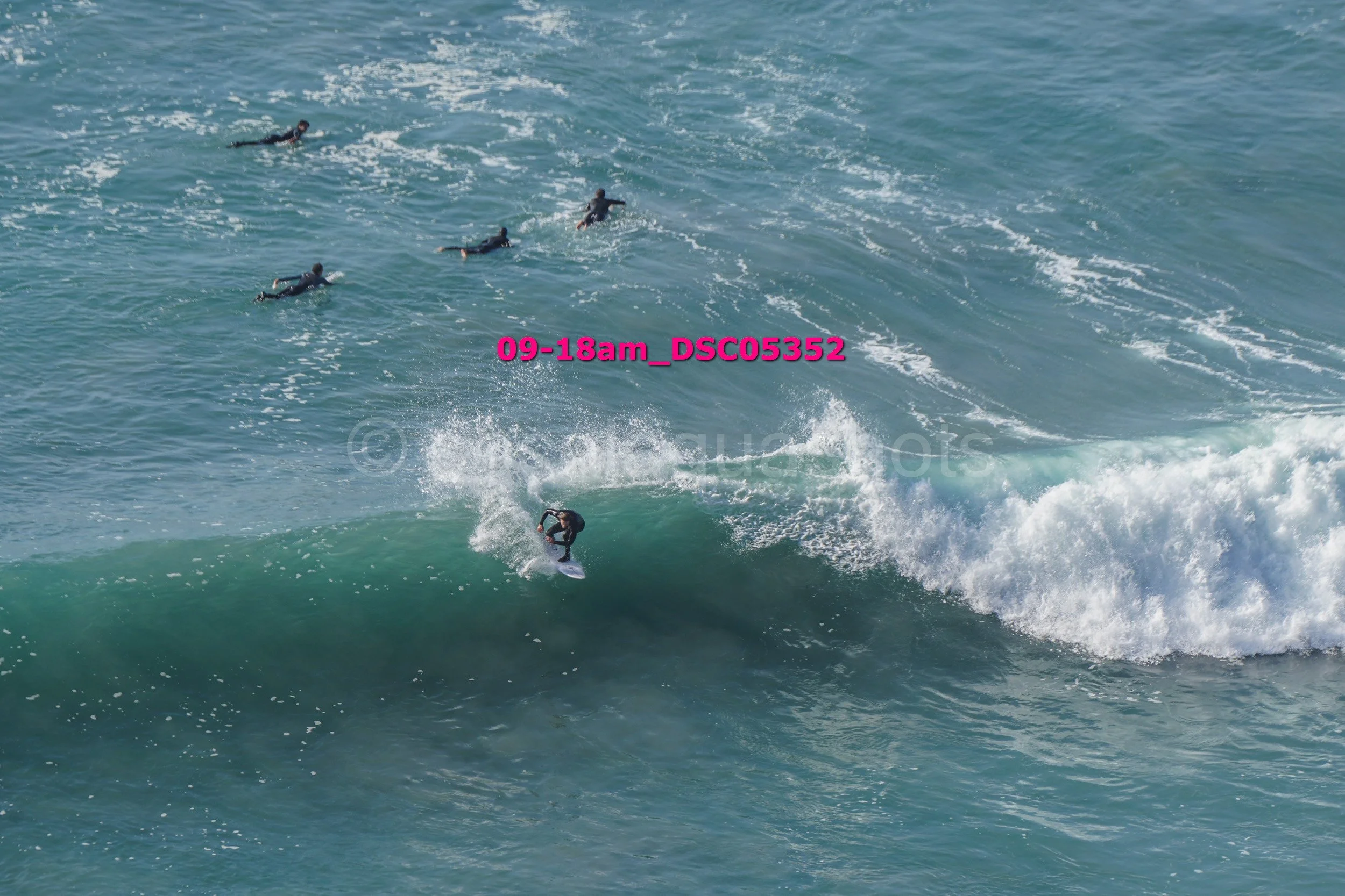 A person surfing on a wave in the ocean with four other surfers visible in the water.