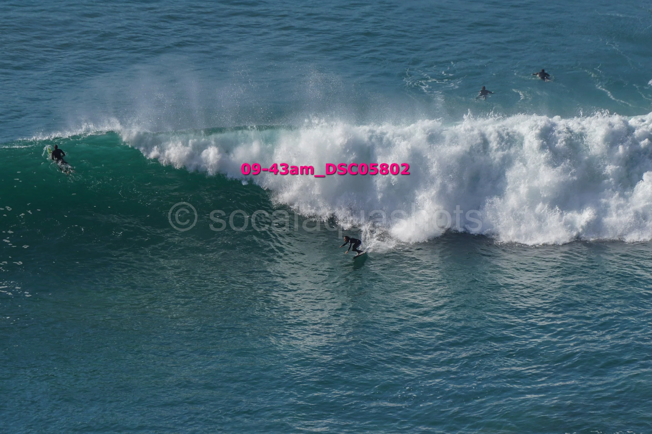 Several surfers riding and paddling on large ocean waves during daytime.