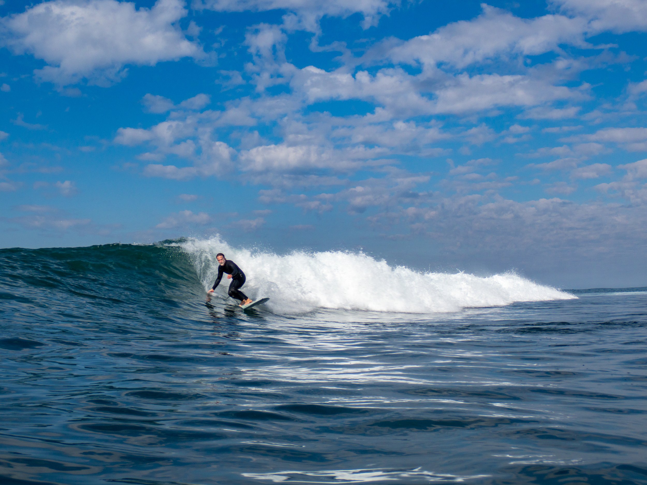 A person surfing on the ocean waves under a partly cloudy sky.