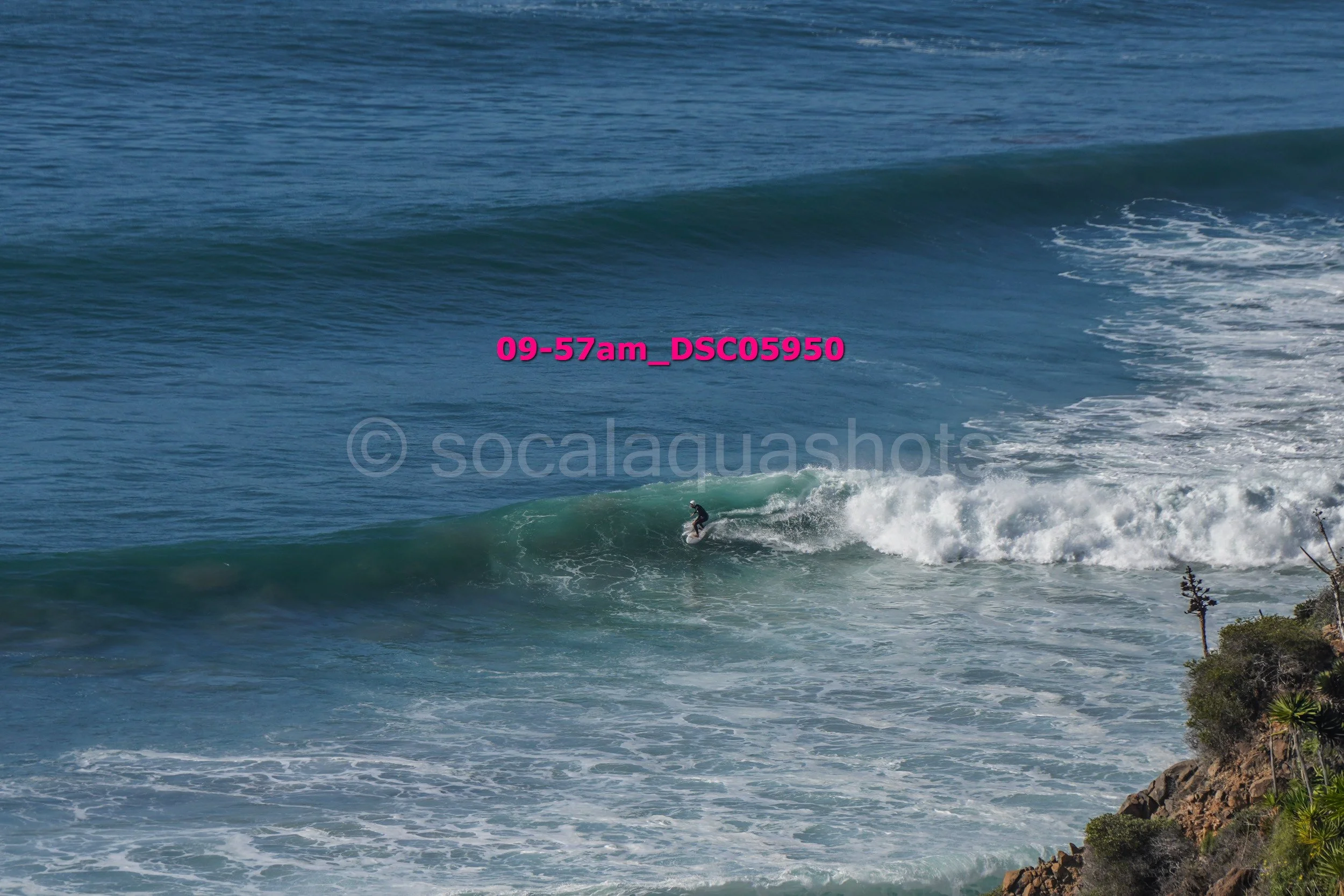 A person surfing on a wave near a rocky shoreline.