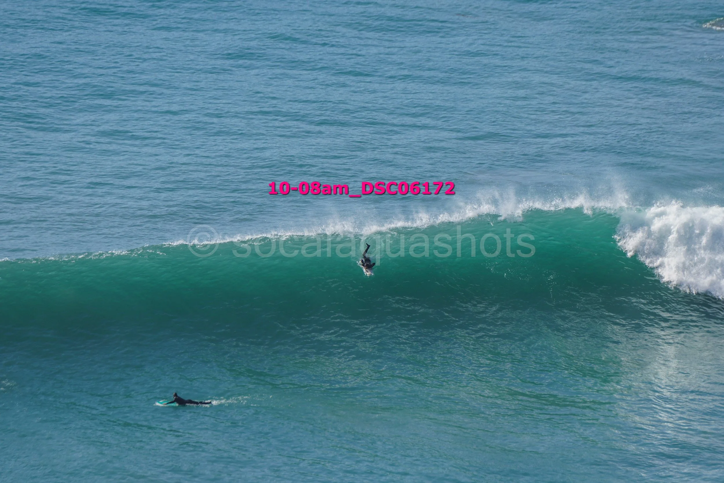 A person surfing a wave in the ocean, with a second swimmer paddling nearby.