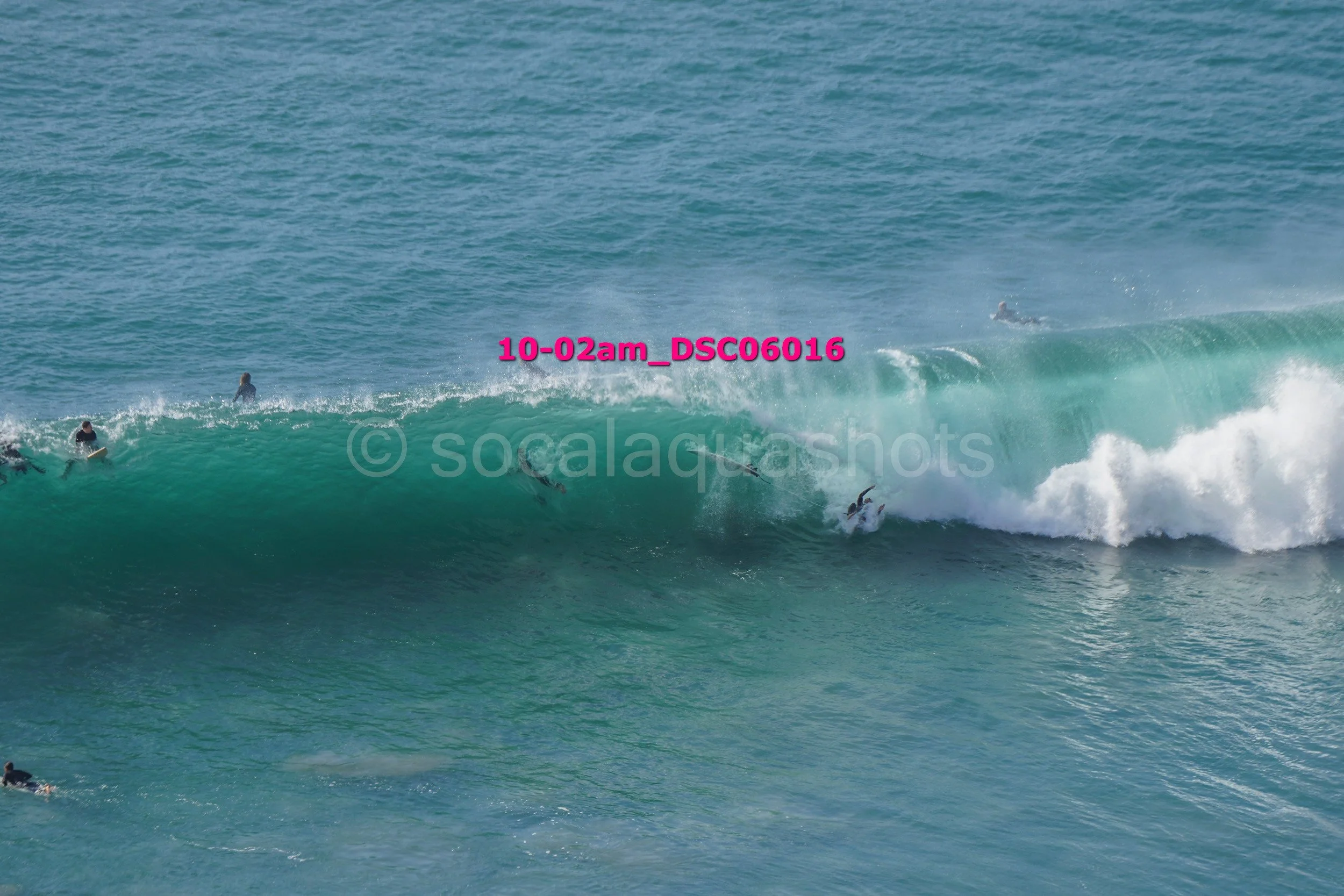 Surfers riding and paddling on a large ocean wave with blue water background.