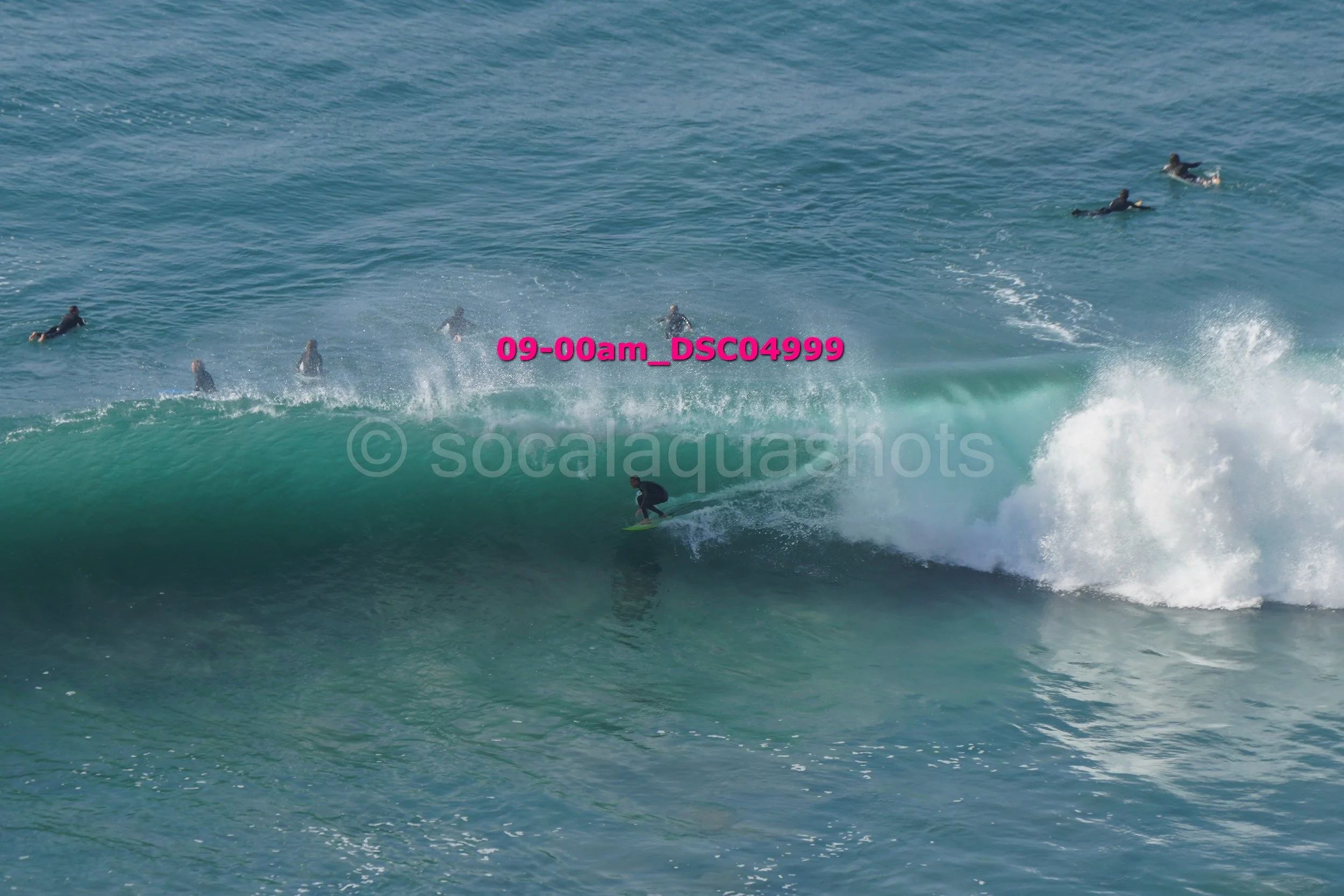 Surfer riding a wave at the beach with several other people swimming and surfing in the background.