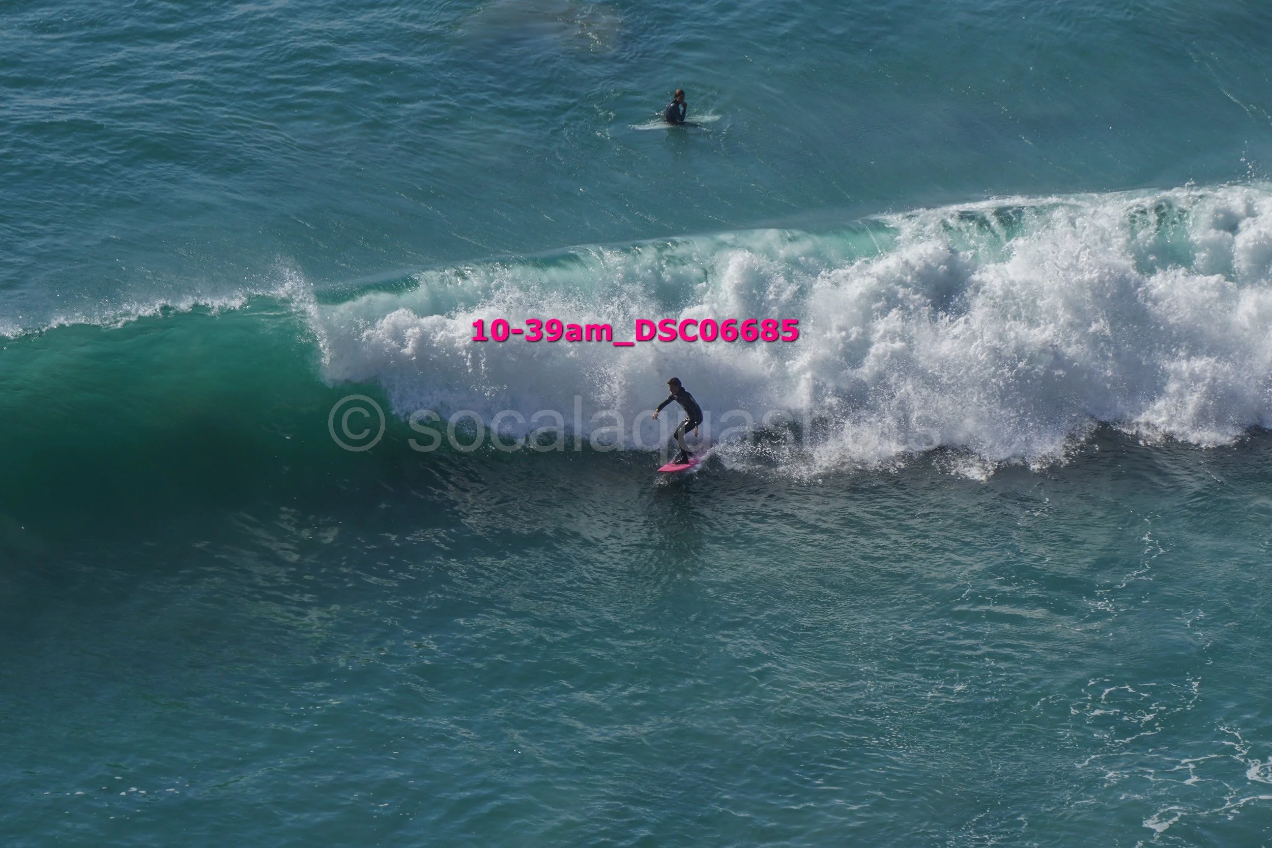 A person surfing on a wave with another surfer in the distance in the ocean.