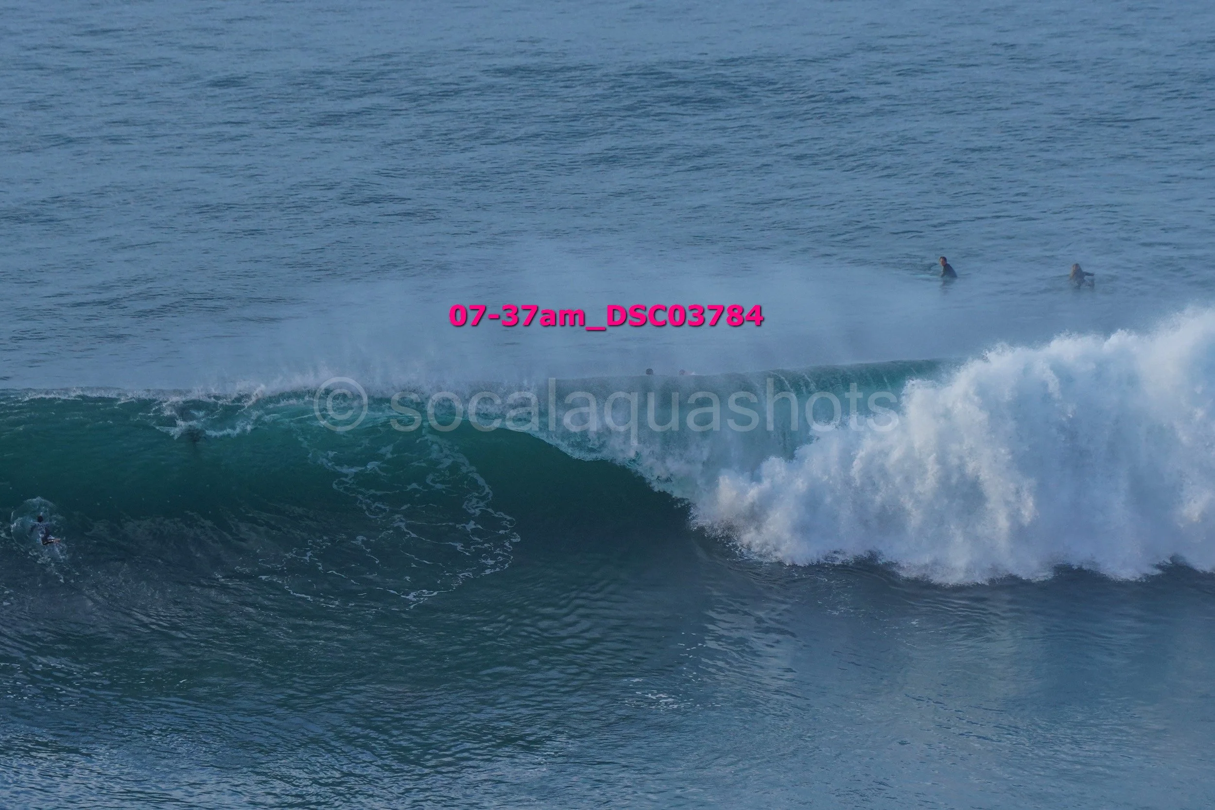 People surfing in the ocean, with one person riding a wave and two others on surfboards in the background.
