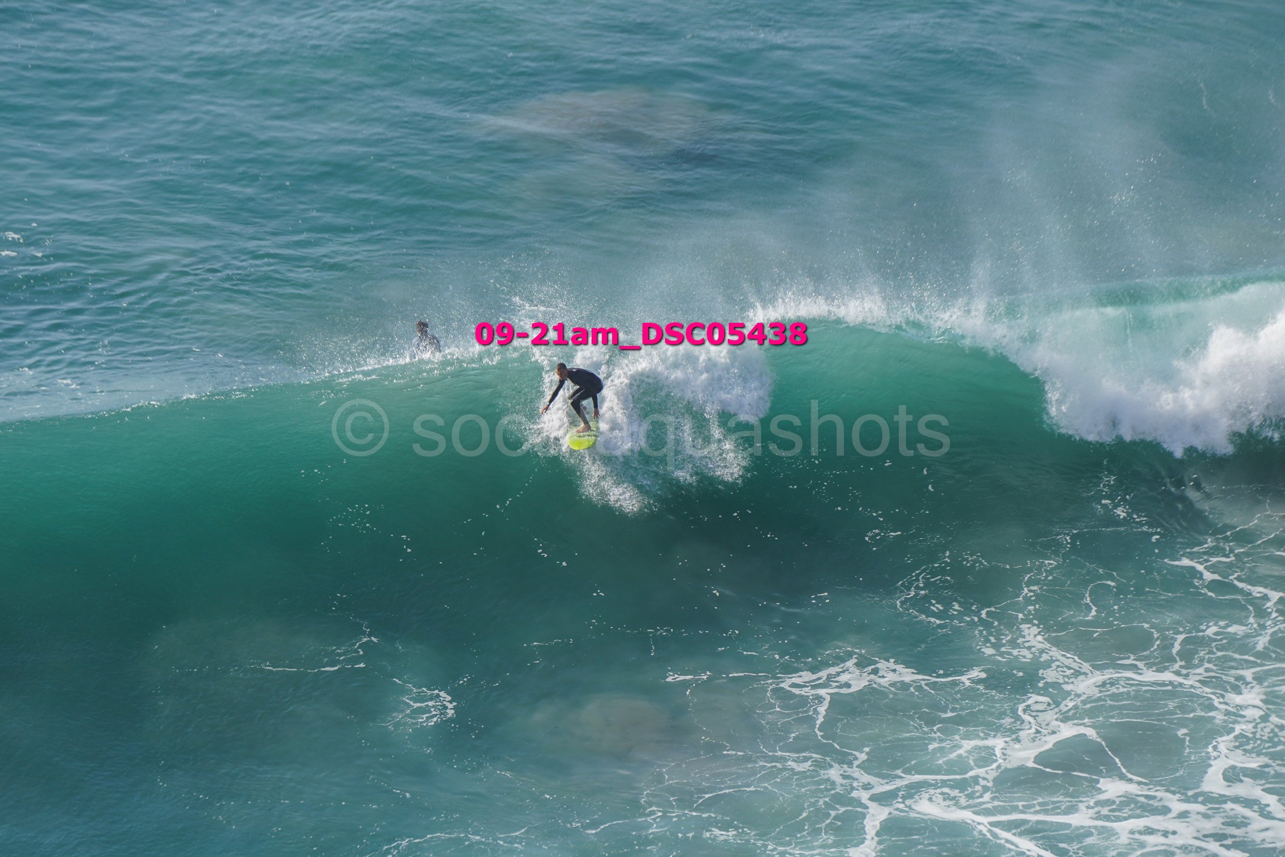 Person surfing on a large ocean wave with two other surfers in the background.