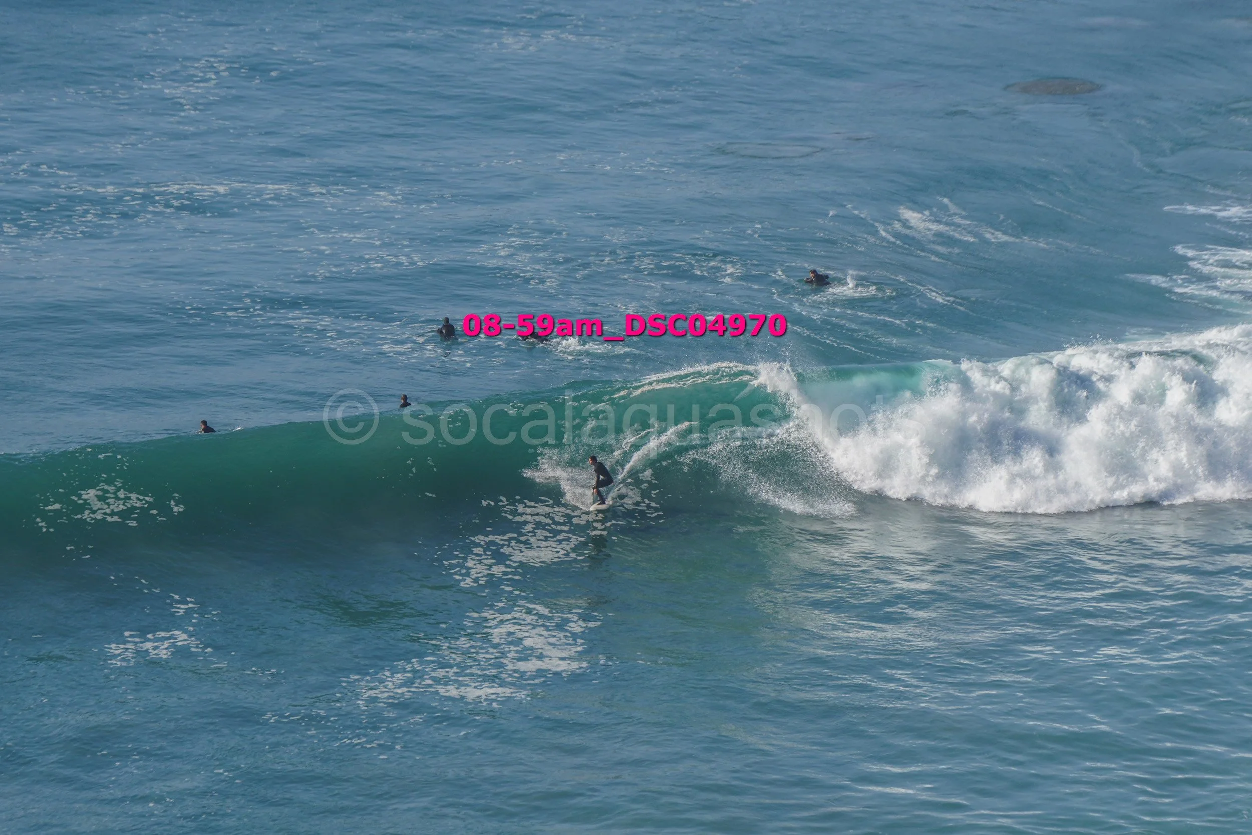 Surfer riding a wave in the ocean with several surfers in the water nearby.