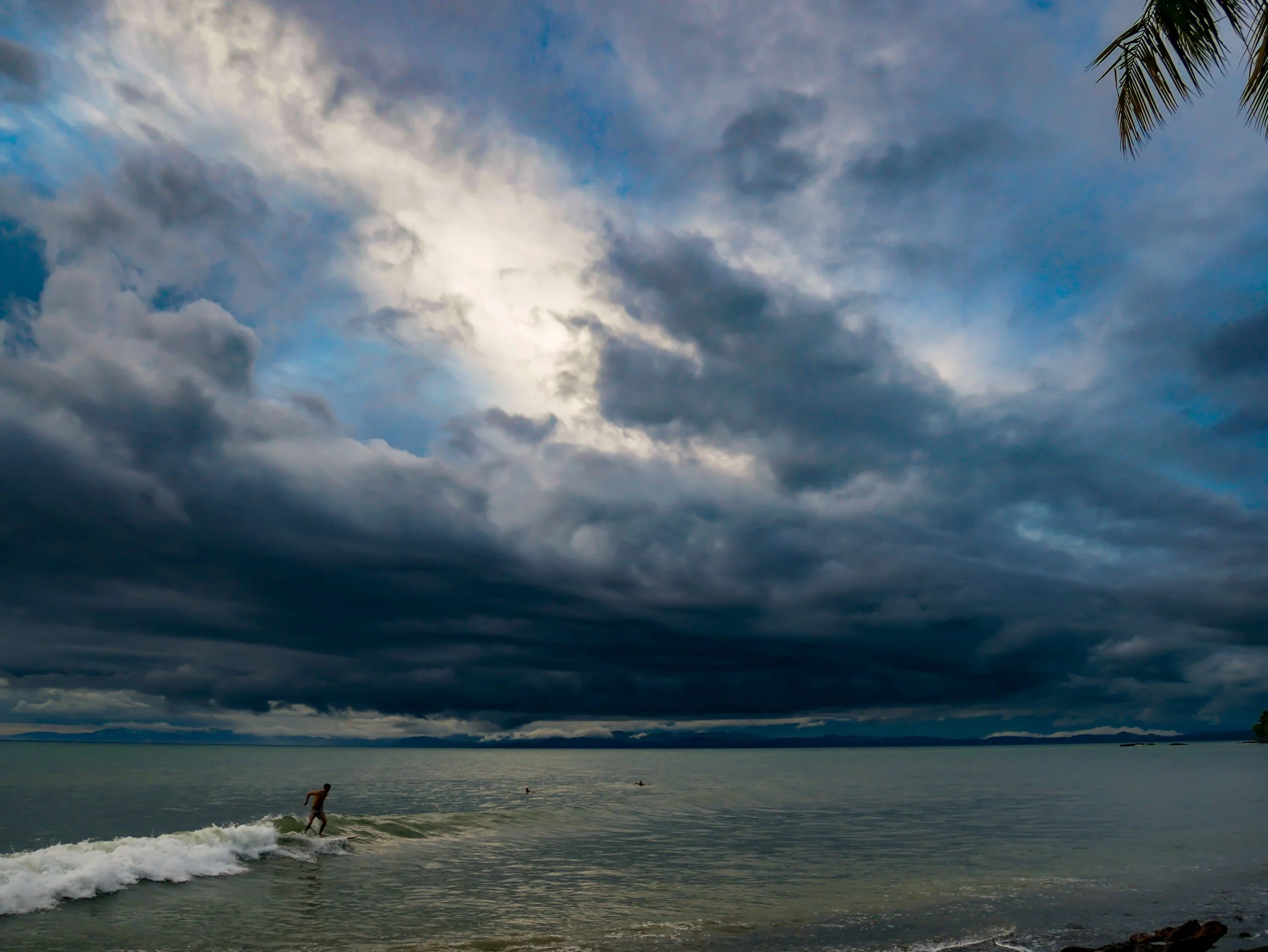 Person surfing on waves under dramatic cloudy sky