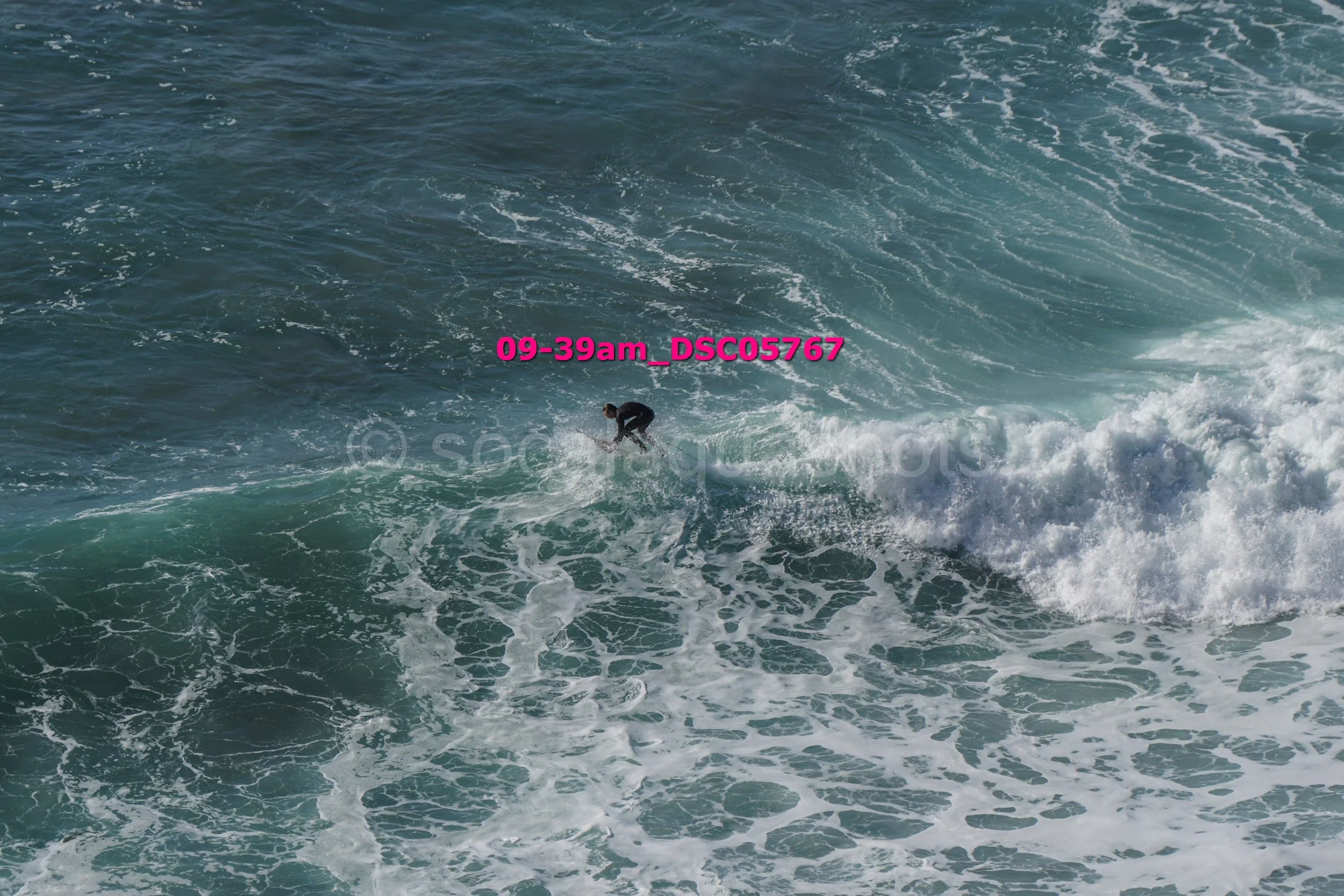 A person surfing on a wave in the ocean, with frothy white surf and deep blue water.