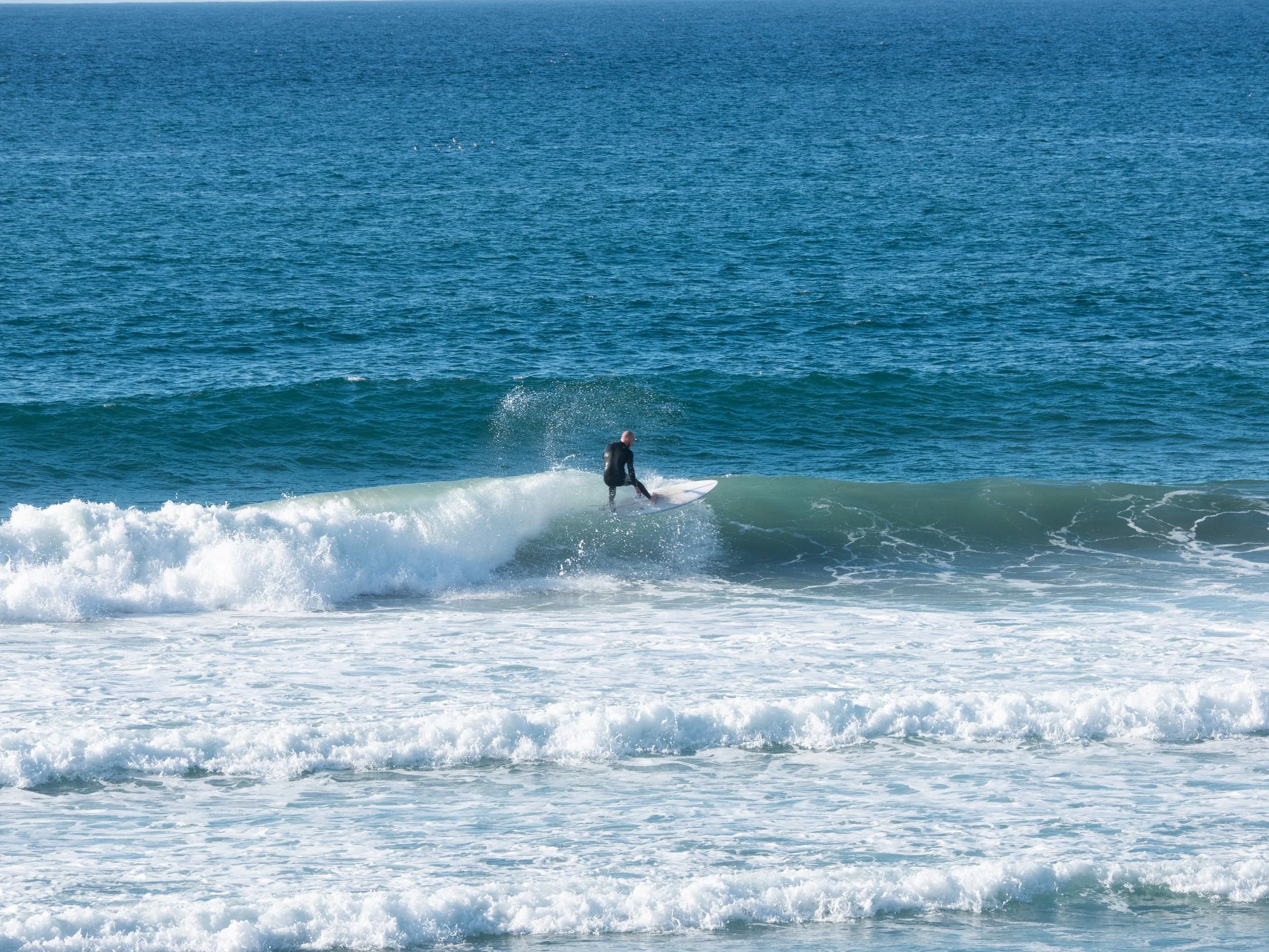 A person surfing on a wave in the ocean with blue water and white surf.