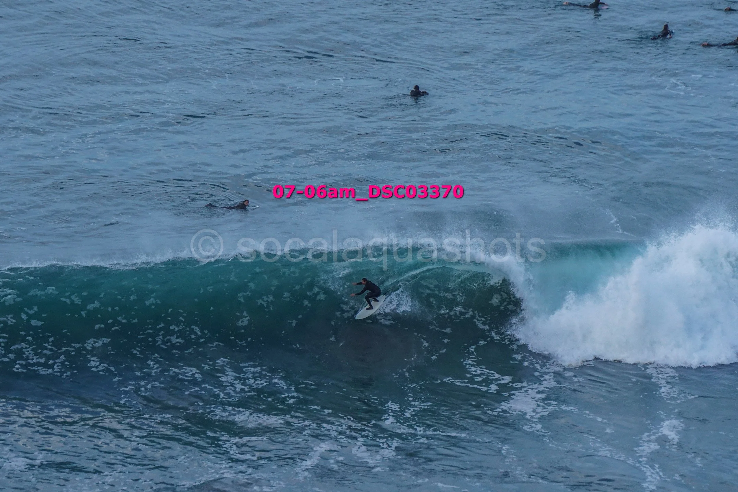 Surfer riding a wave near a group of swimmers in the ocean.