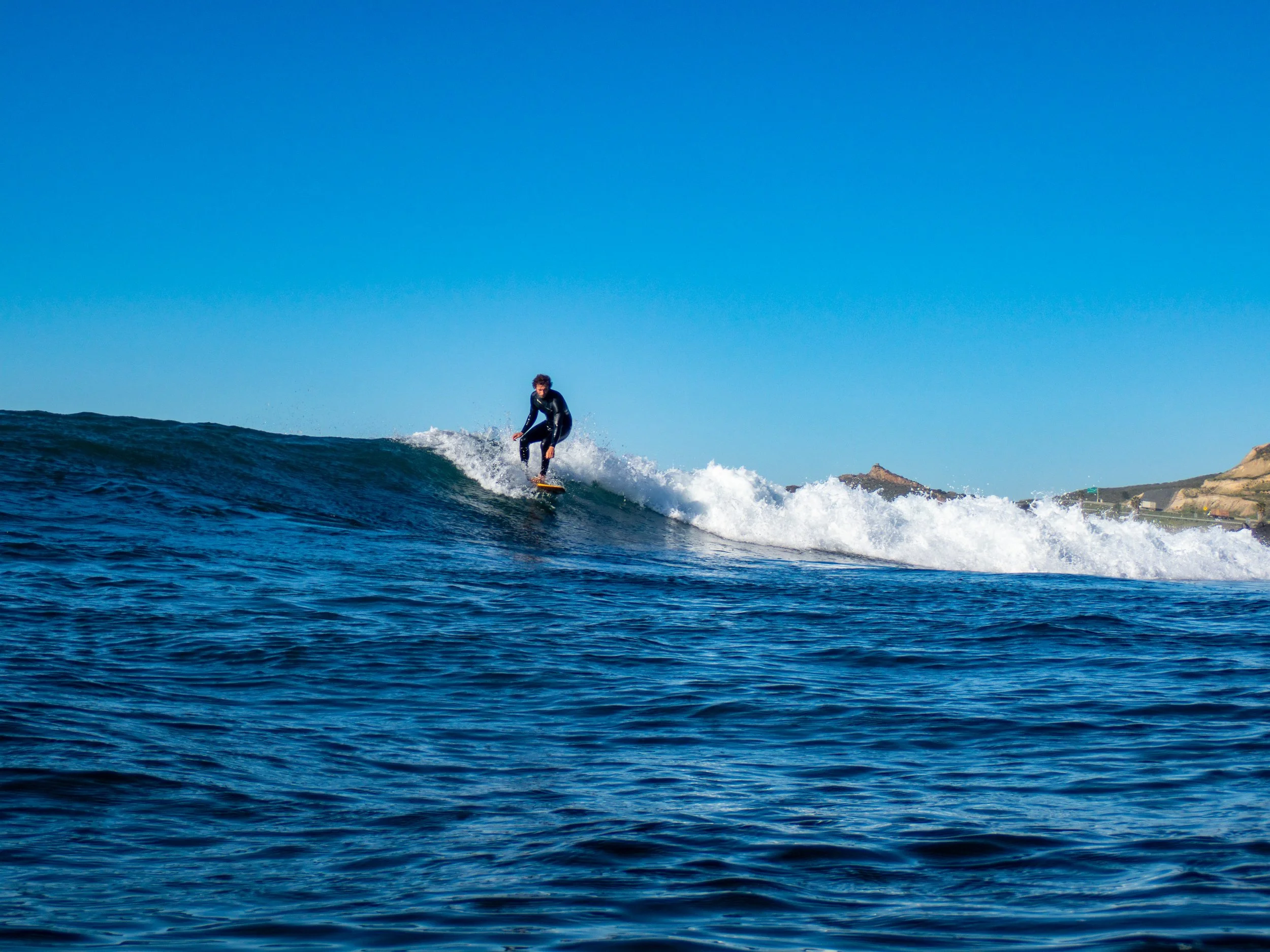A person surfing on a wave in the ocean on a clear day with a blue sky.
