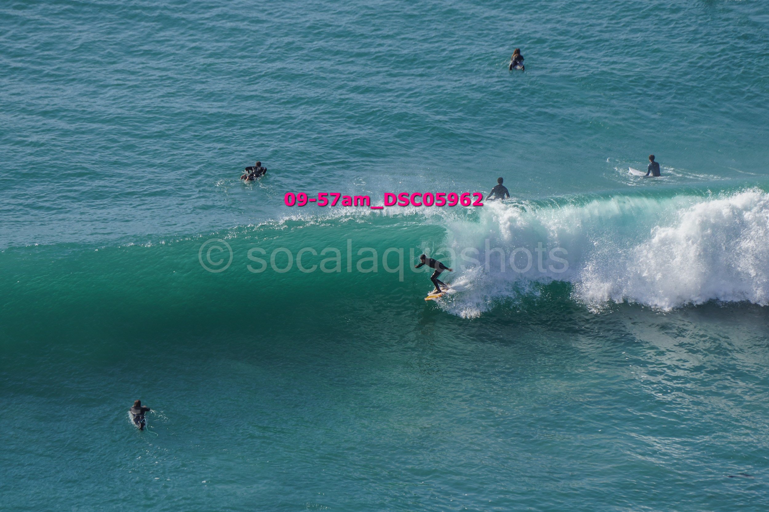 Surfer riding a wave with several people in the water around.