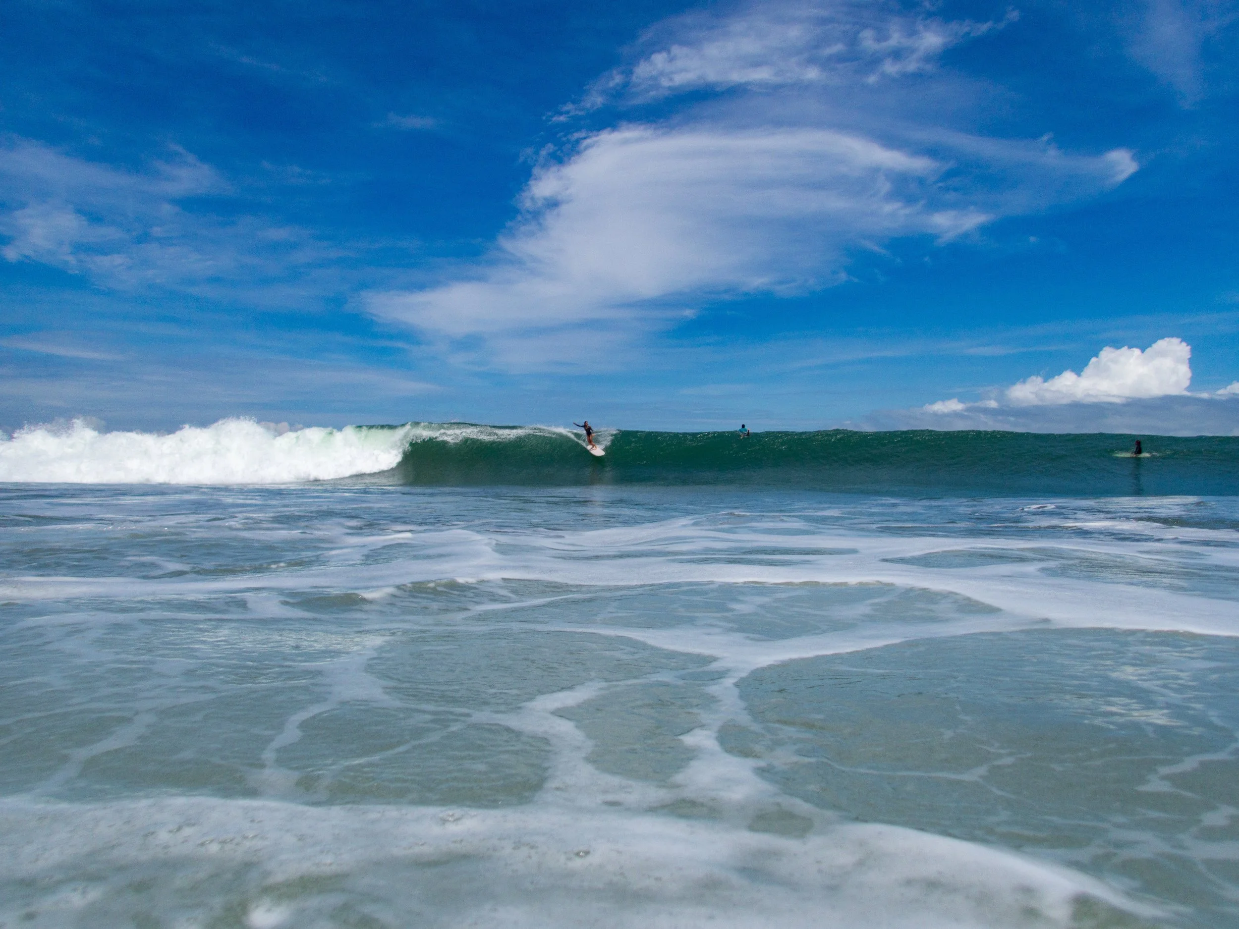 Ocean wave with surfers on a clear day under blue skies