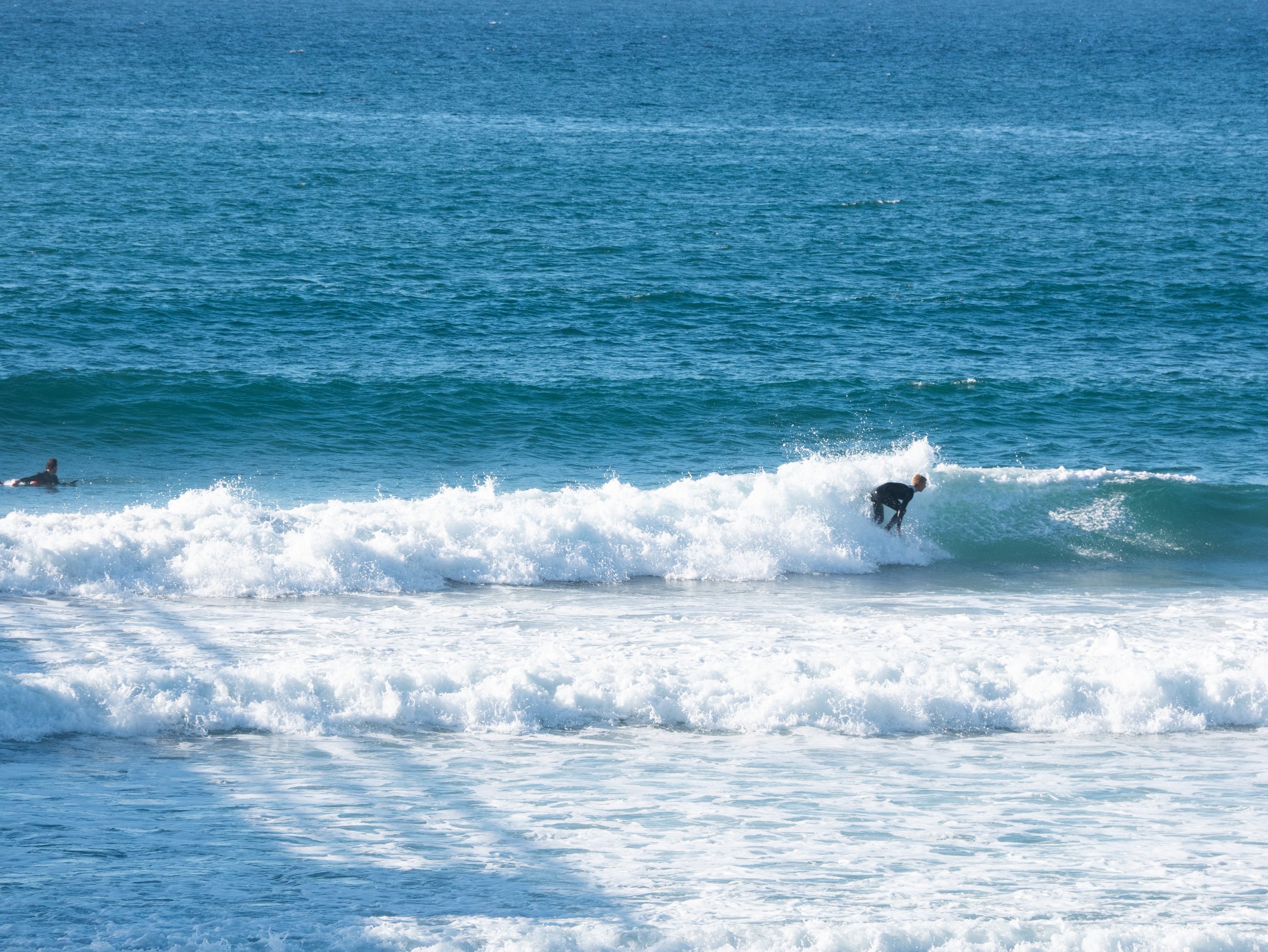 A person surfing on a wave in the ocean with another surfer visible in the background.
