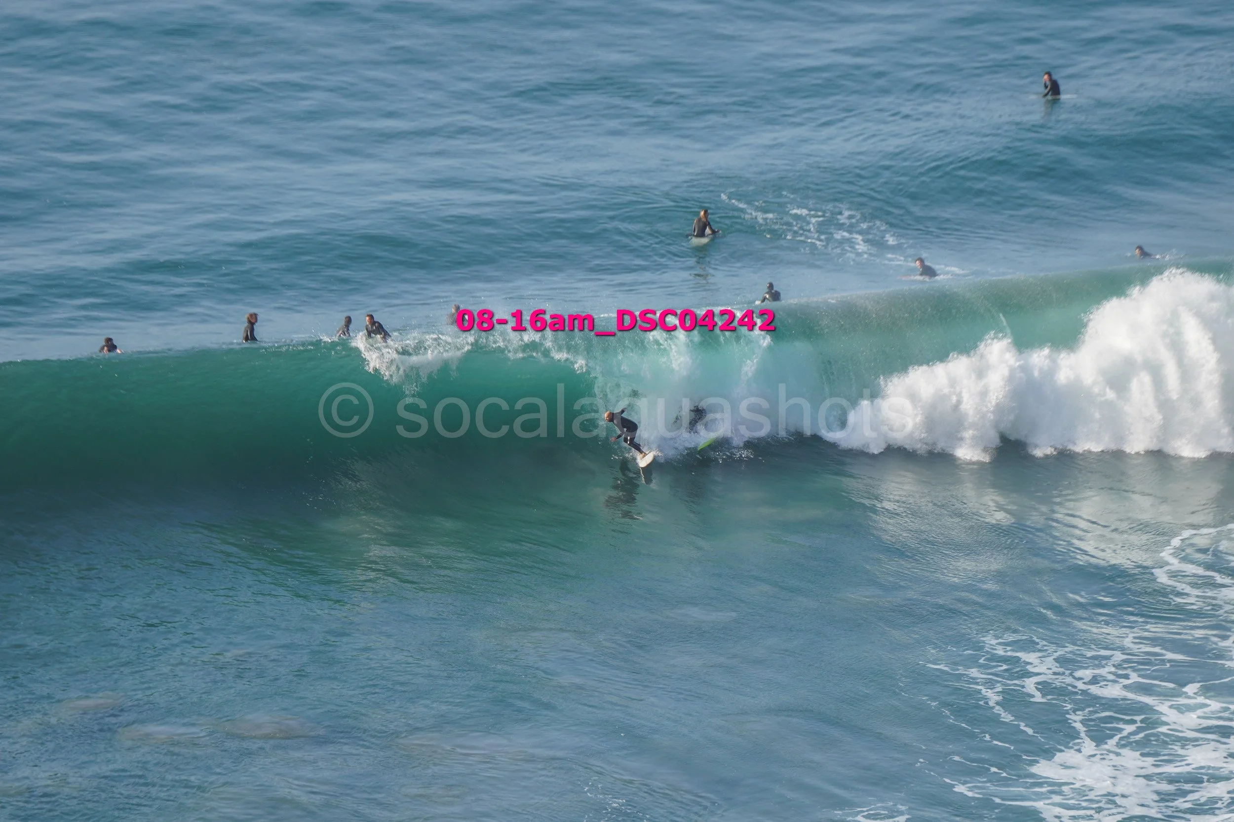 Surfer riding a large wave with multiple surfers in the water in the background.