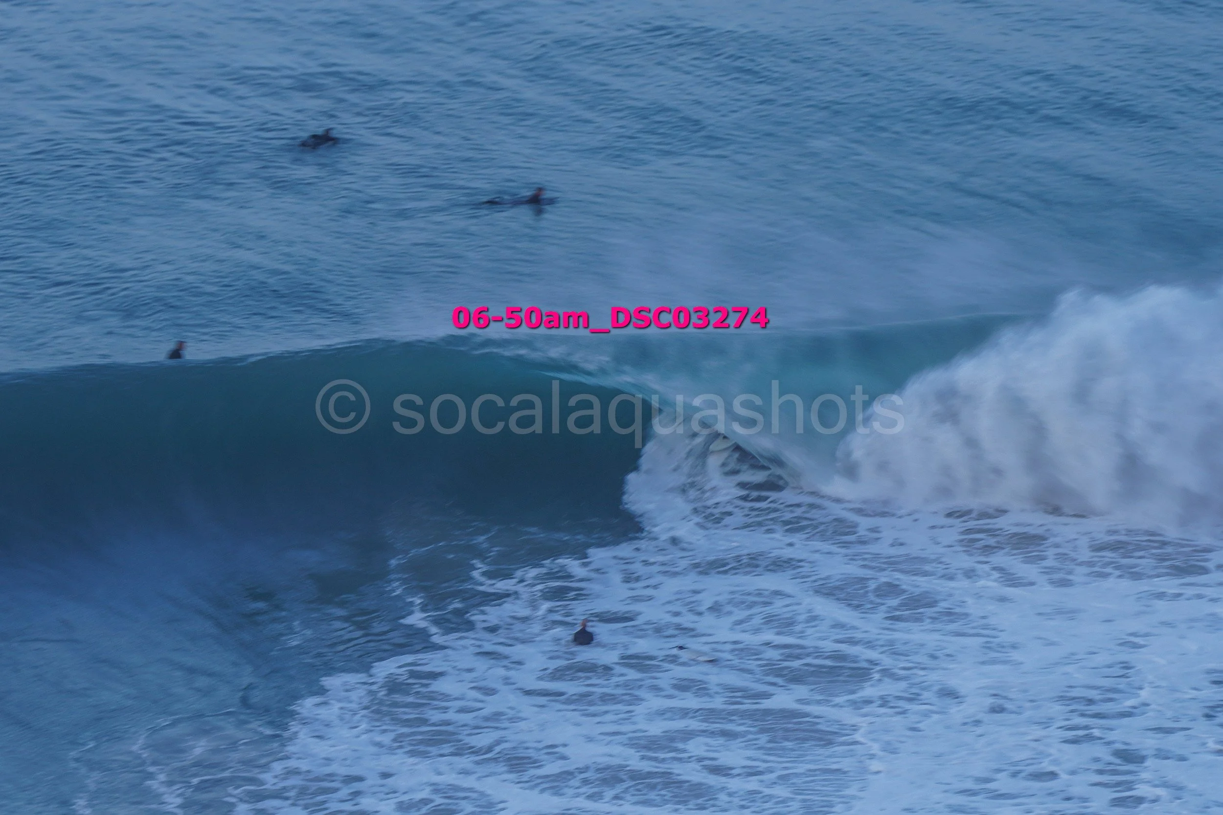 Ocean waves with surfers in the water, large wave breaking with white foam, and surfer riding the wave.