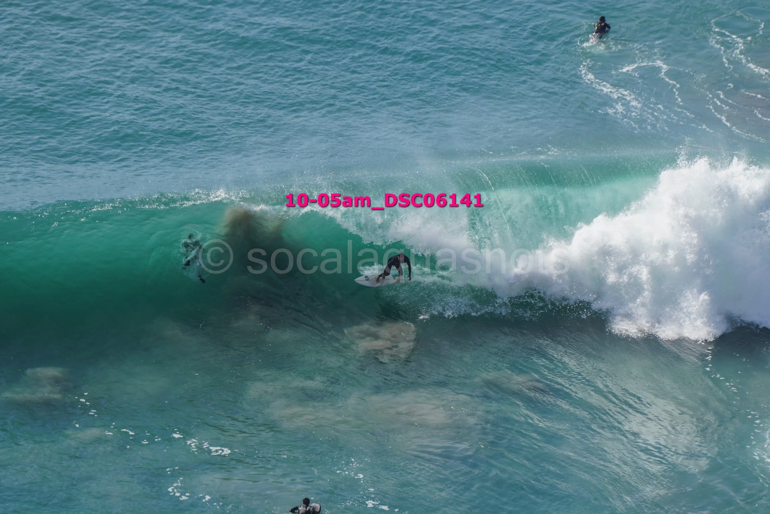 Surfer riding a large wave in the ocean with another surfer in the background and a person in the water underneath.