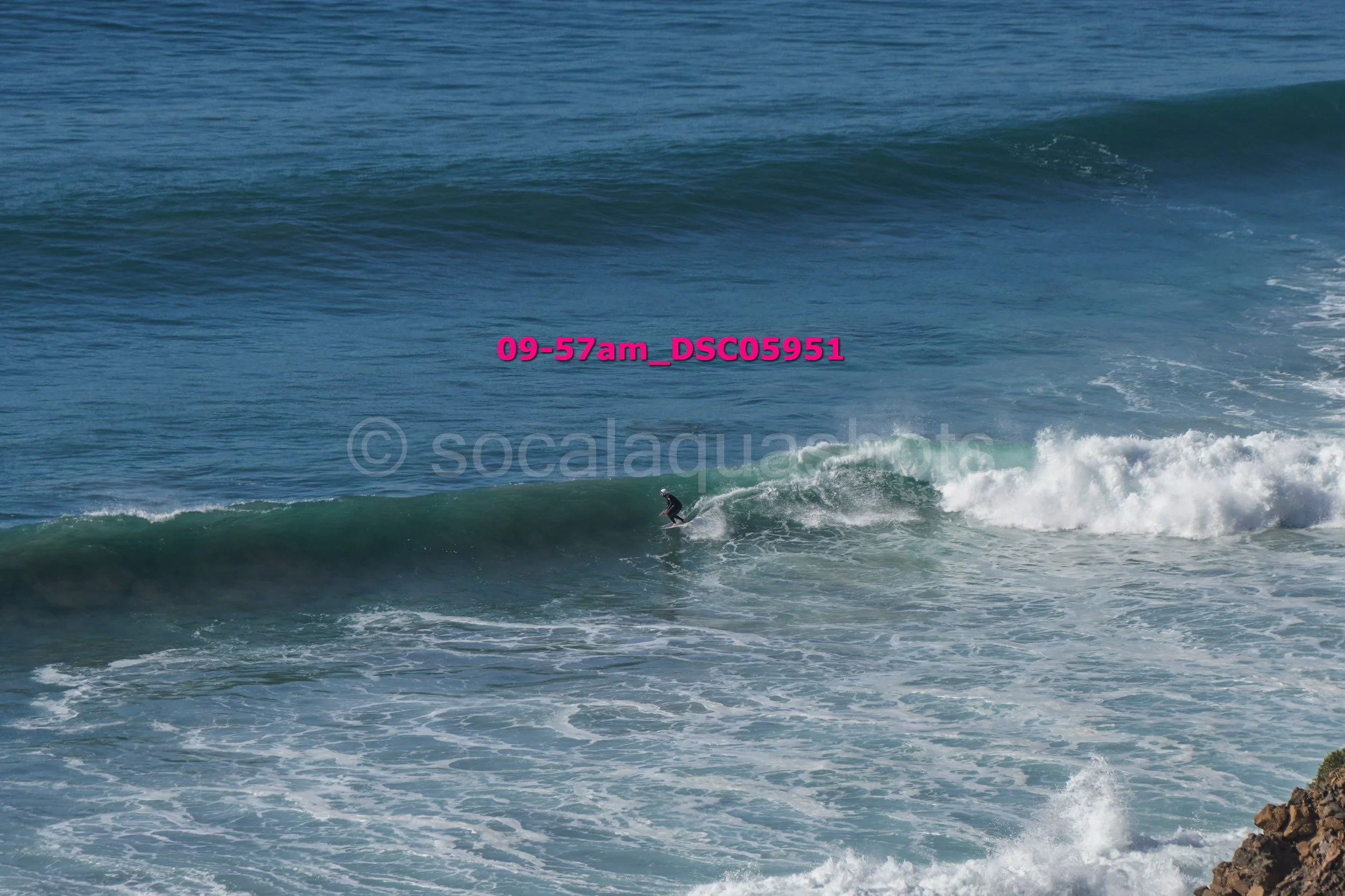 A lone surfer riding a wave in the ocean near a rocky shoreline.