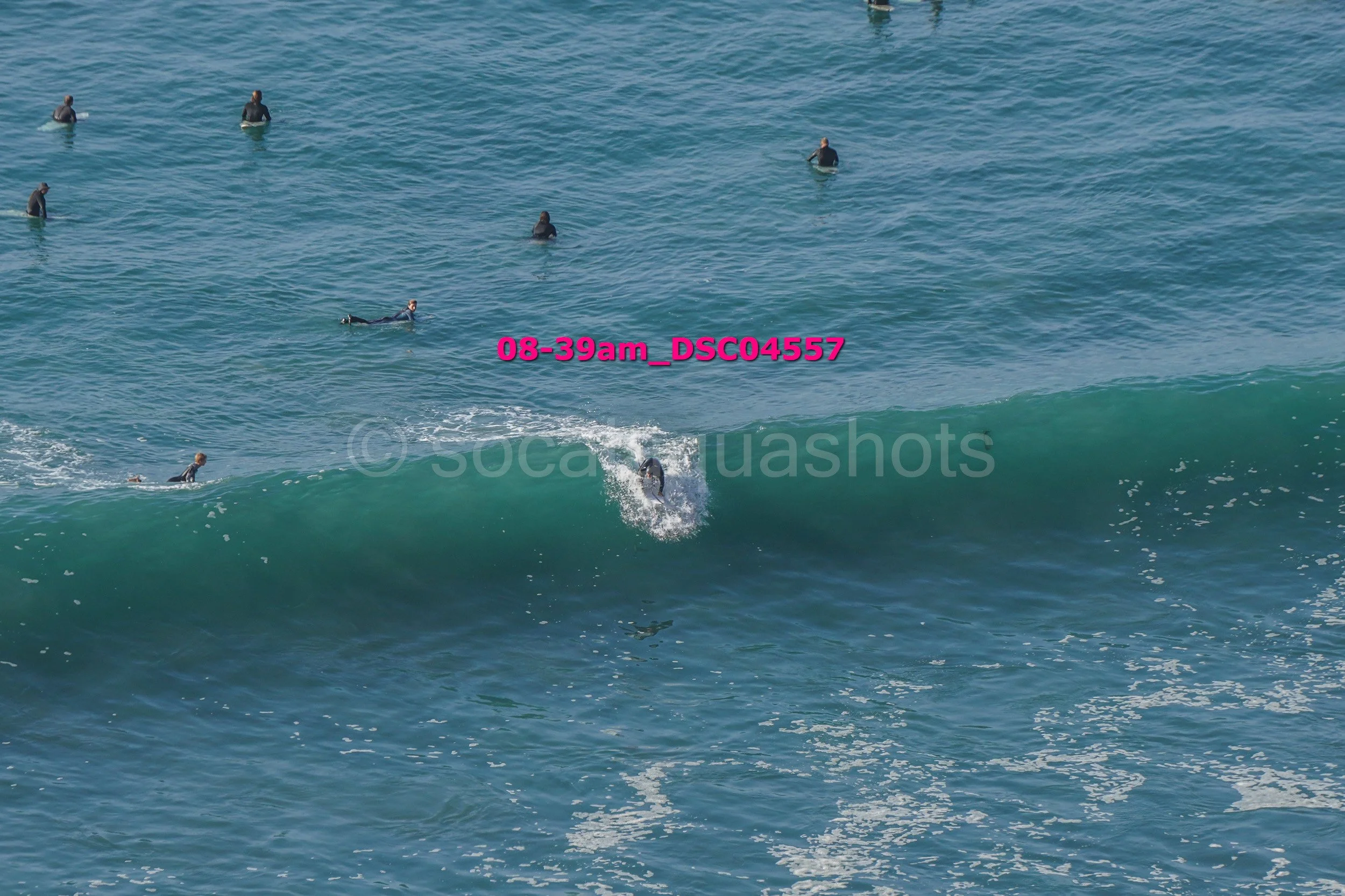 Surfboarder riding a wave in the ocean with several surfers in the background.