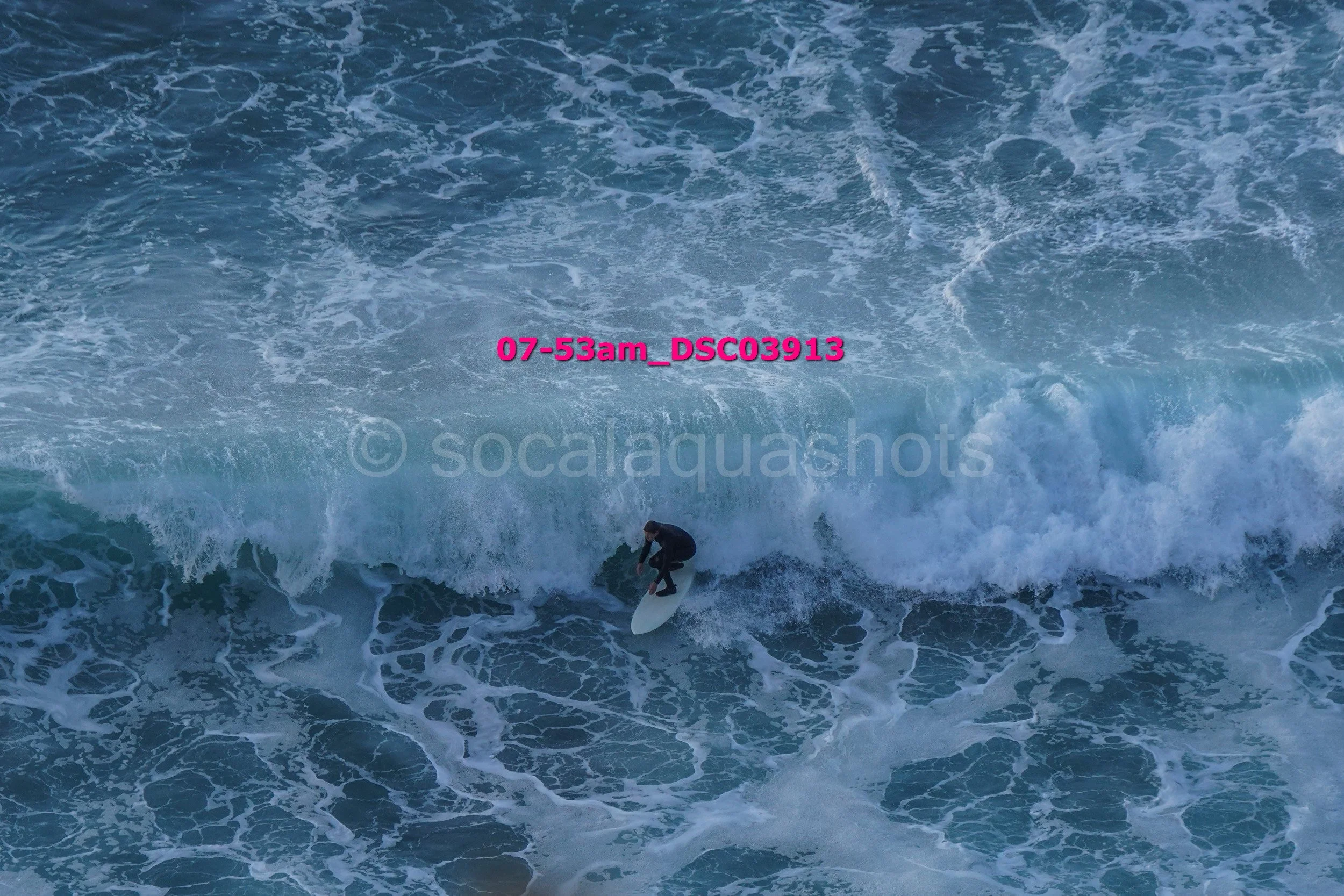 A surfer in a black wetsuit riding a wave in the ocean, with white foam surrounding them.