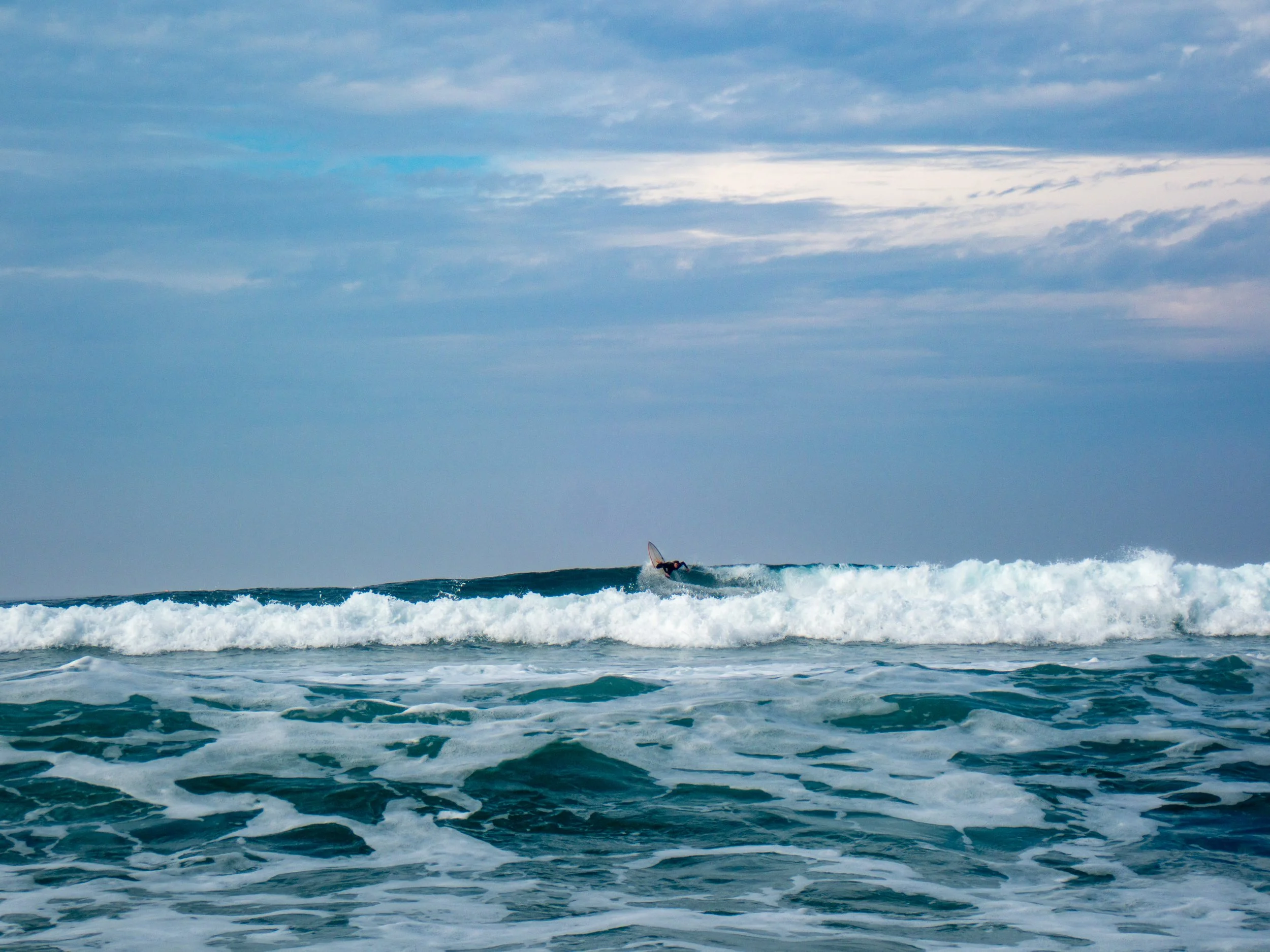 A person surfing on a wave in the ocean under a cloudy sky.