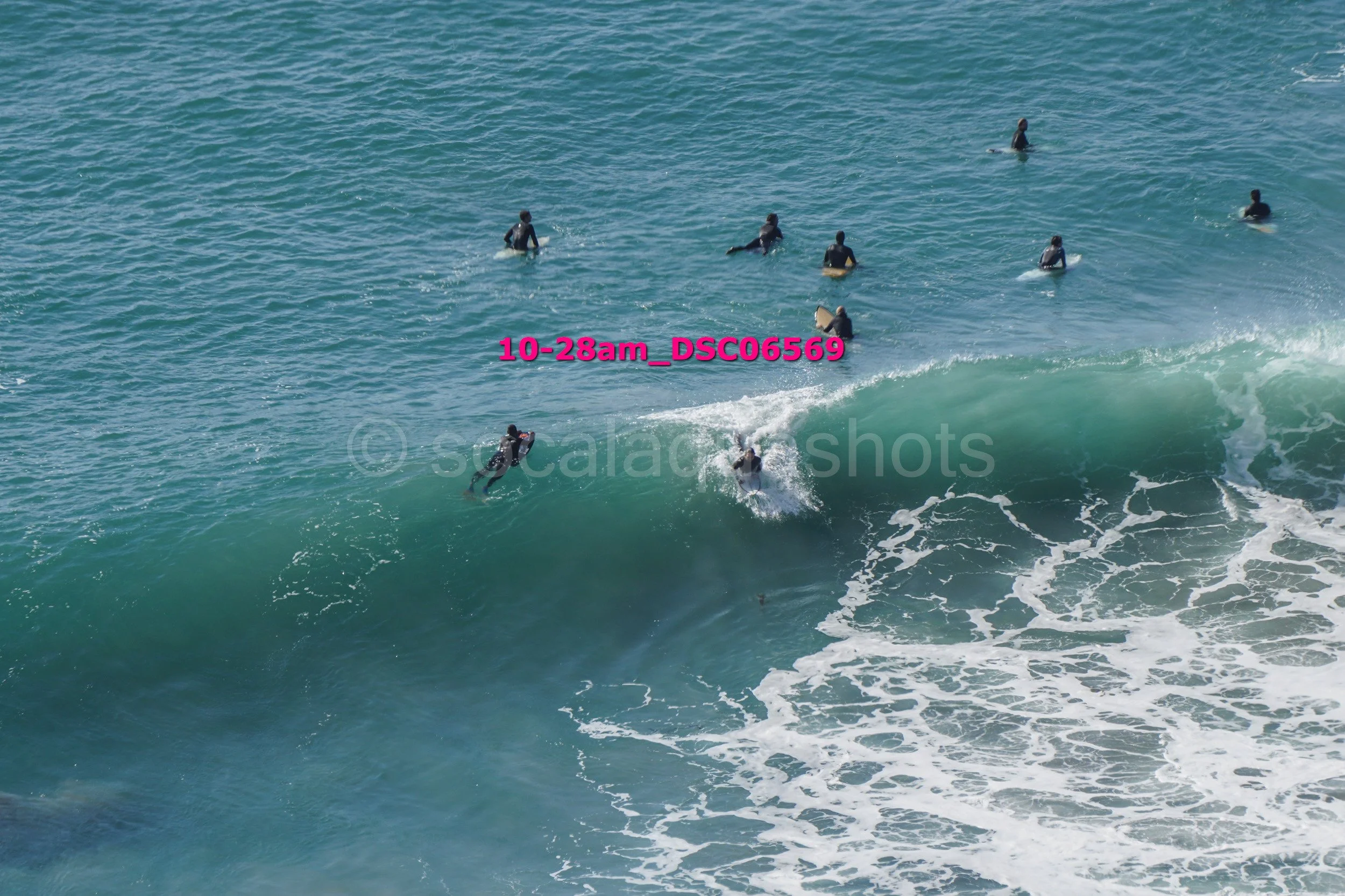 Surfers in black wetsuits riding a wave and paddling in the ocean.