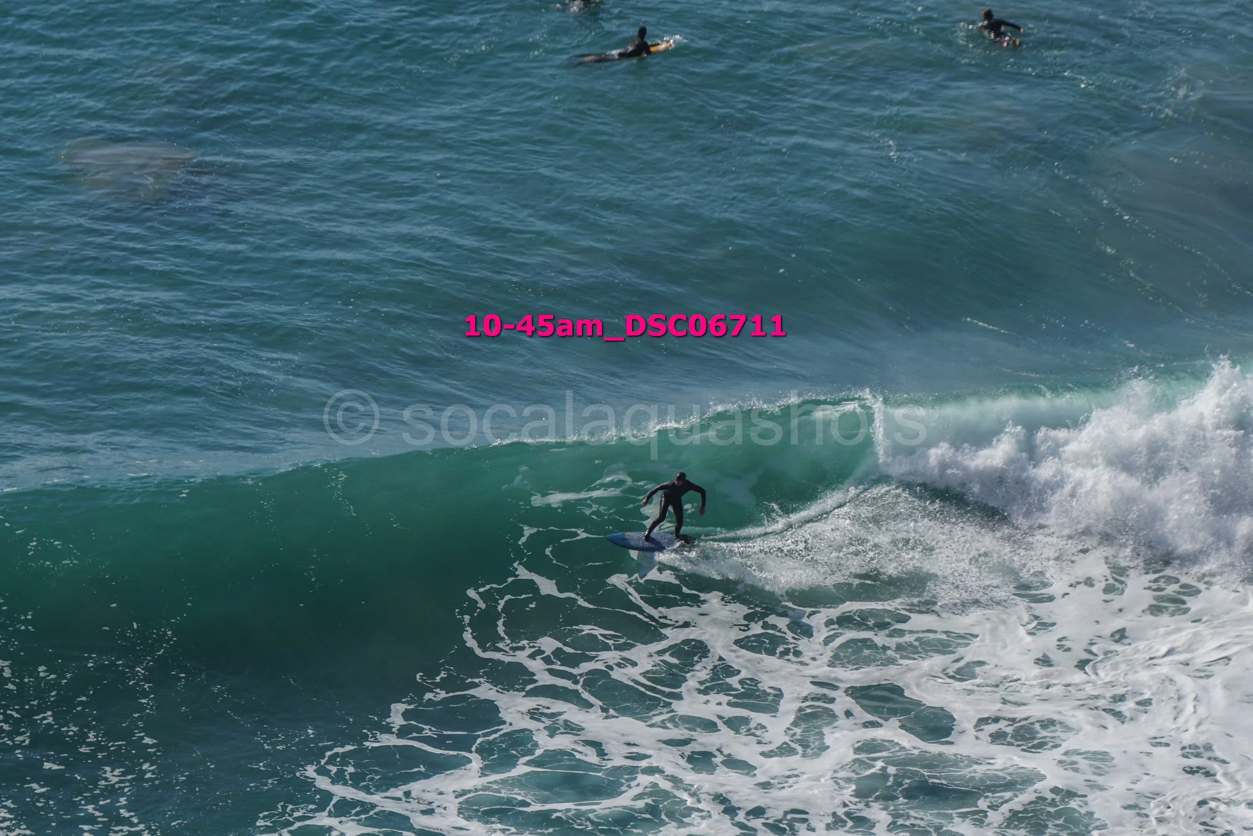Surfer riding a wave in the ocean with other surfers in the background.