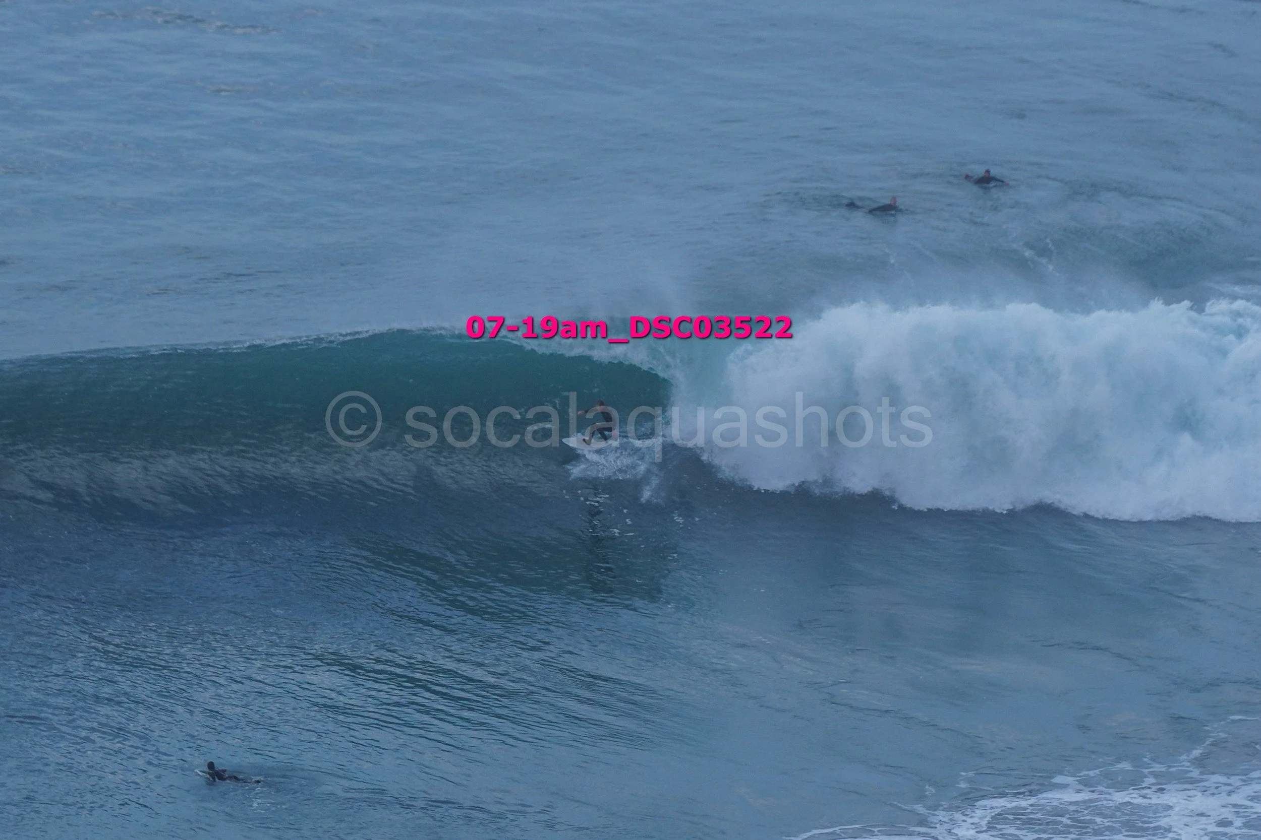 A person surfing on a wave with several other surfers visible in the ocean nearby.